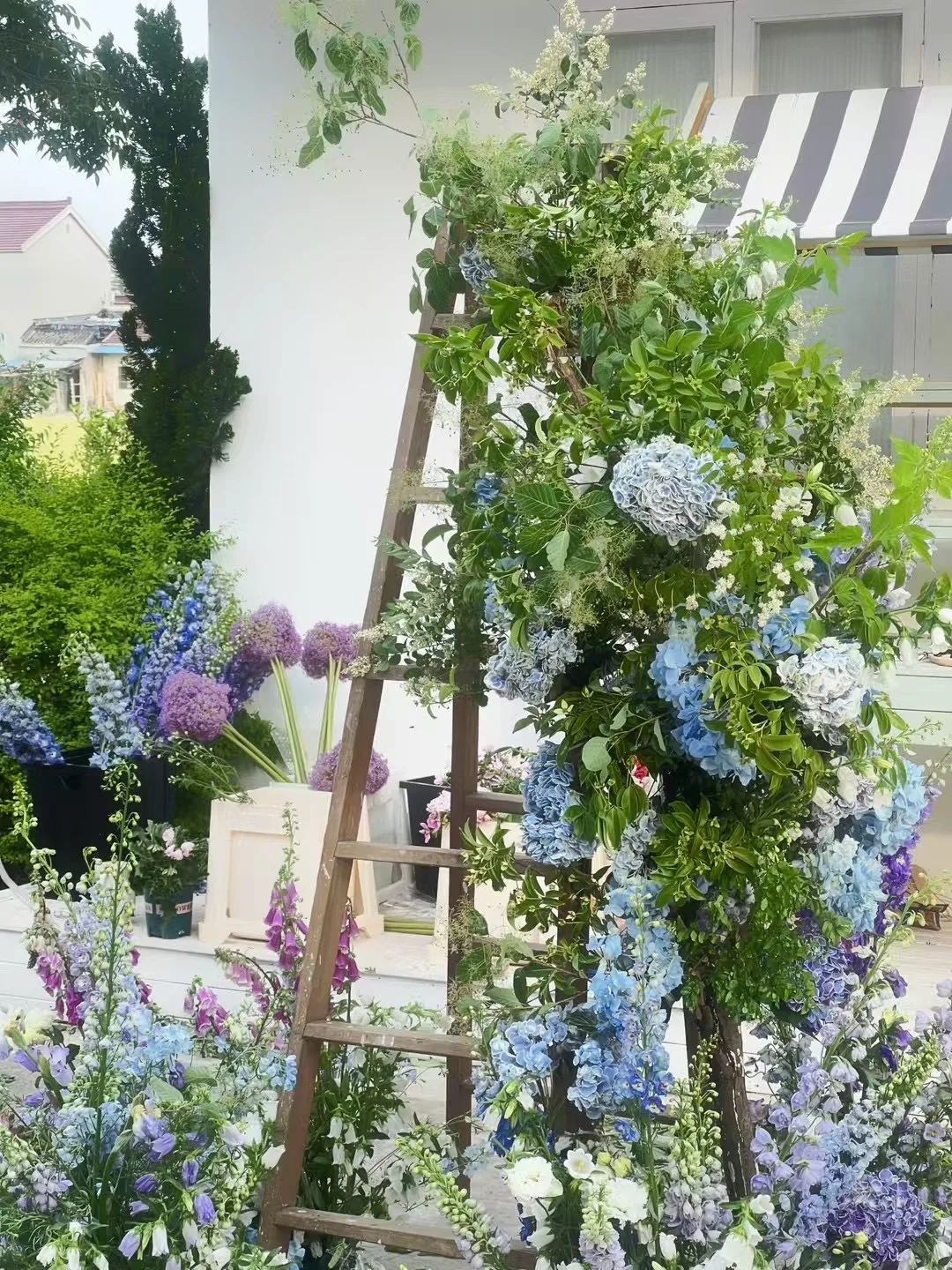 Blue and lavender floral installation of hydrangeas and delphiniums built on a wooden ladder outdoors