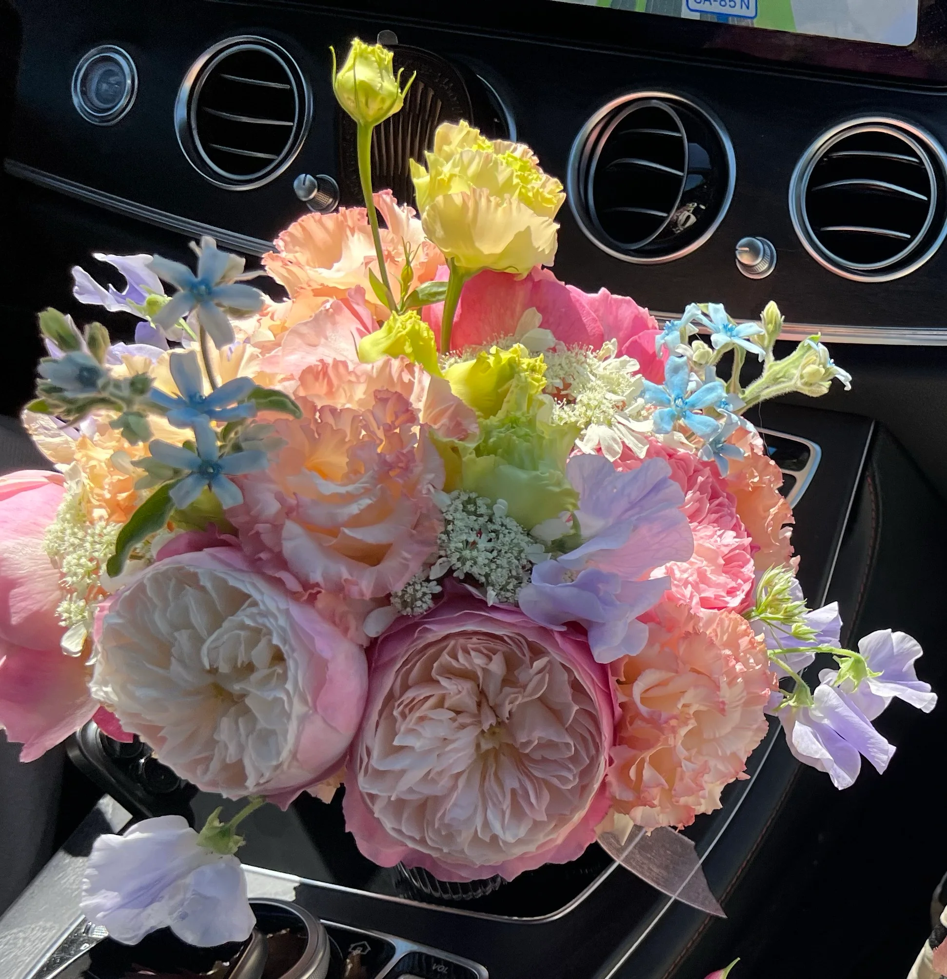 Pastel bouquet of garden roses and delicate blue and pink flowers resting on a car console