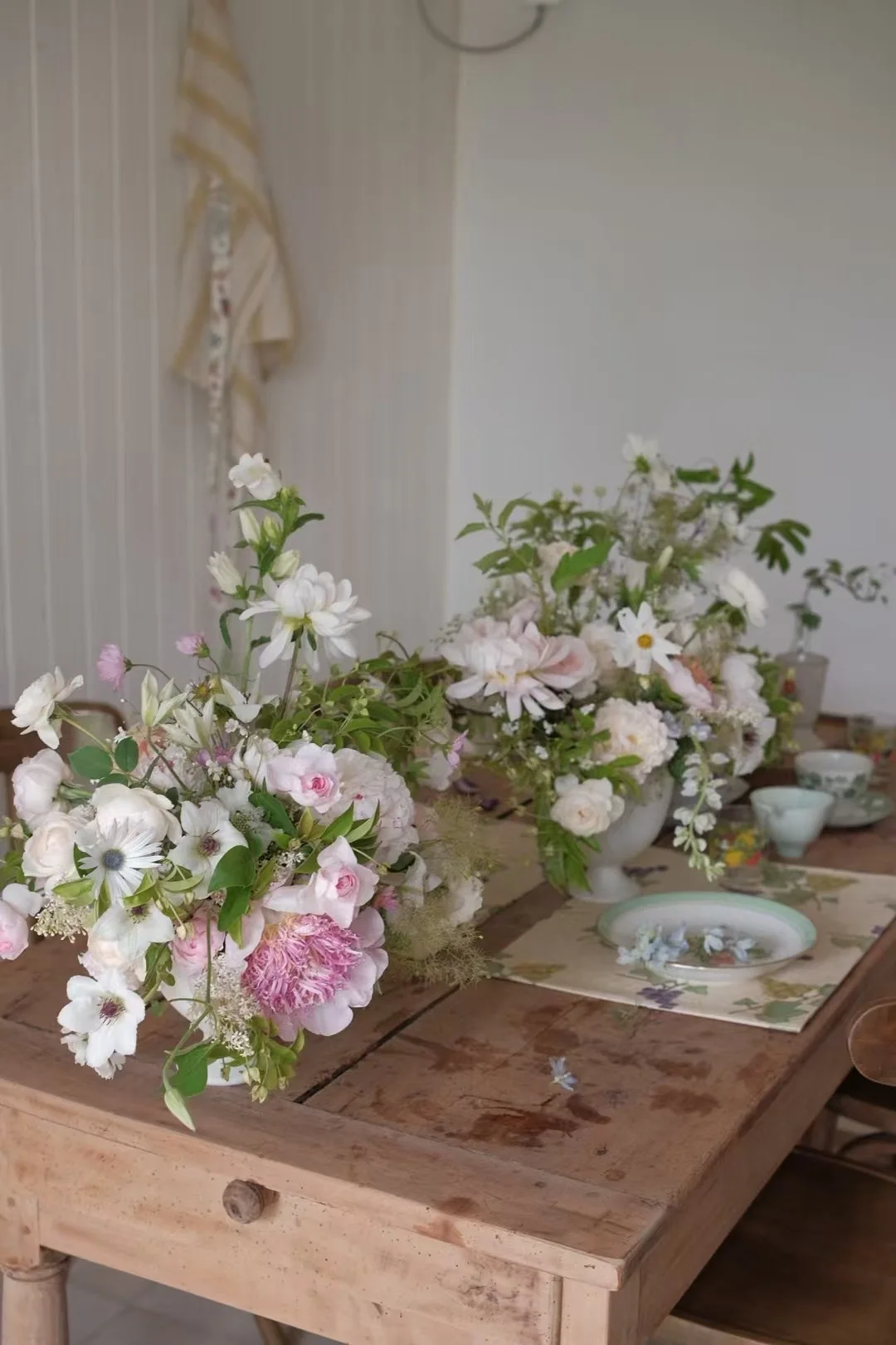 Soft pink and white floral centerpieces on a rustic farmhouse table in a light-filled room
