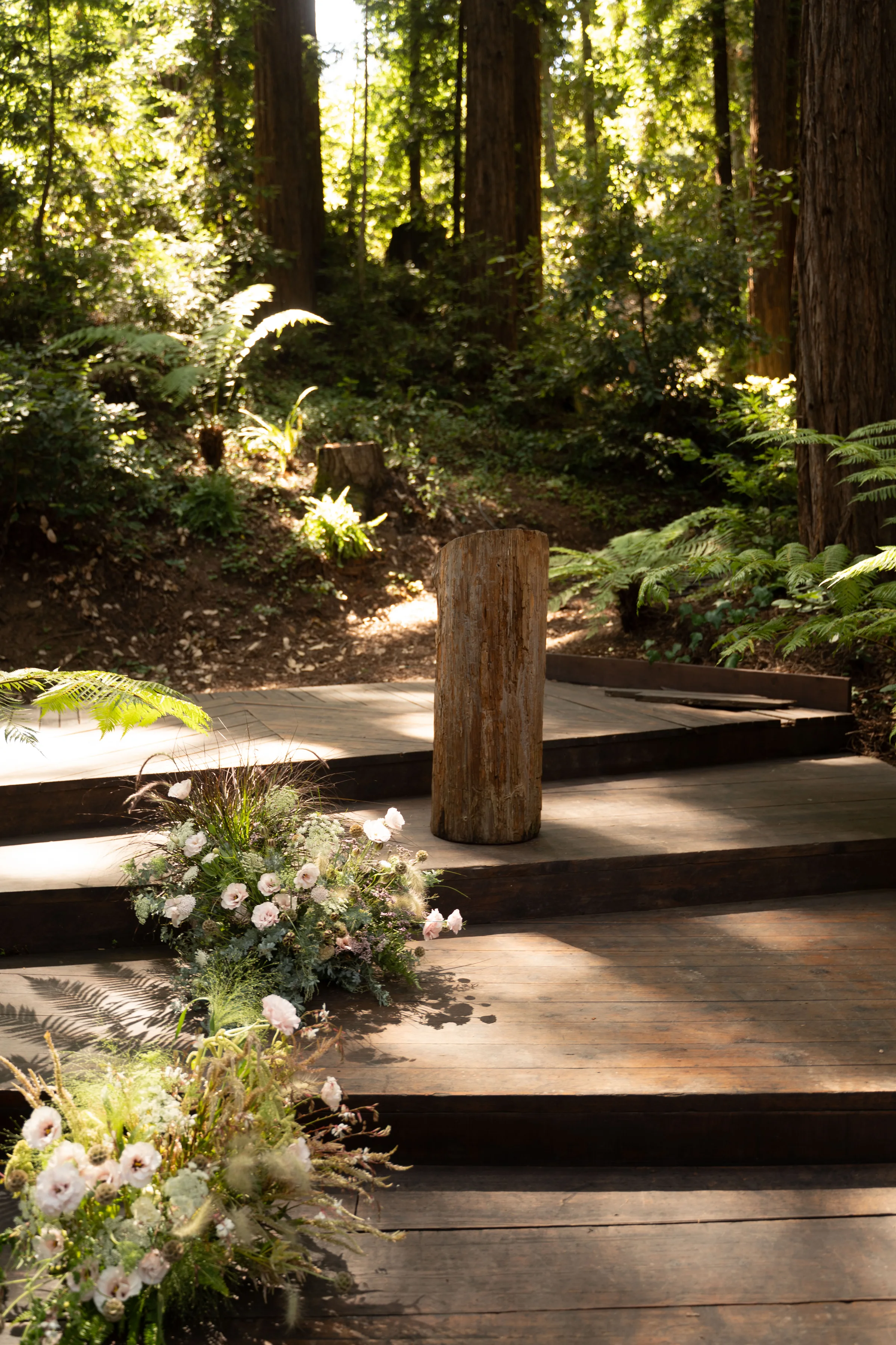Rustic wooden ceremony pedestal and steps surrounded by ferns and delicate flowers in a forest