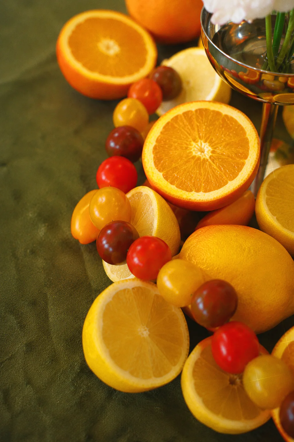 Close detail of cut oranges, lemons, and red and yellow cherry tomatoes arranged on a green tablecloth