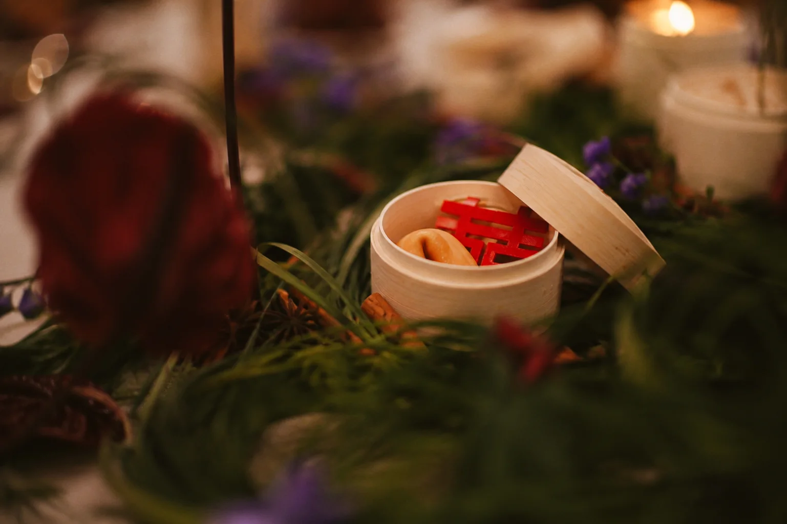 A fortune cookie and red paper decoration in an open bamboo steamer nestled among greenery on a softly lit table
