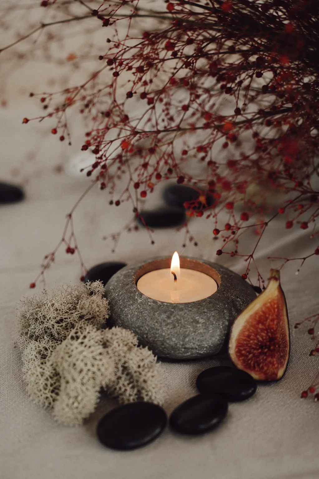 Close detail of a stone candle, fig, preserved moss, black river stones, and red berry stems