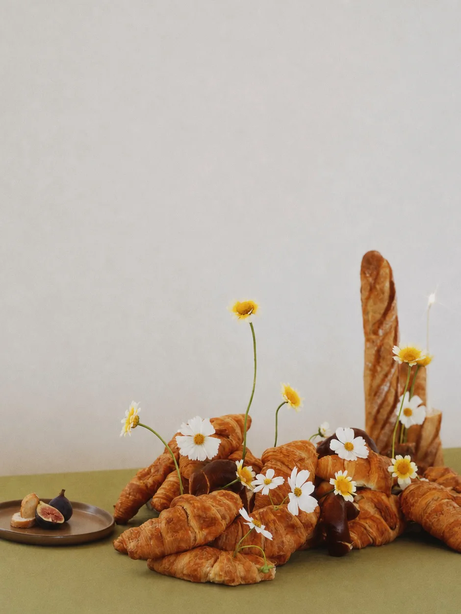 Bread-and-flower arrangement with tall baguettes, piled croissants, white blooms, and a small plate of figs