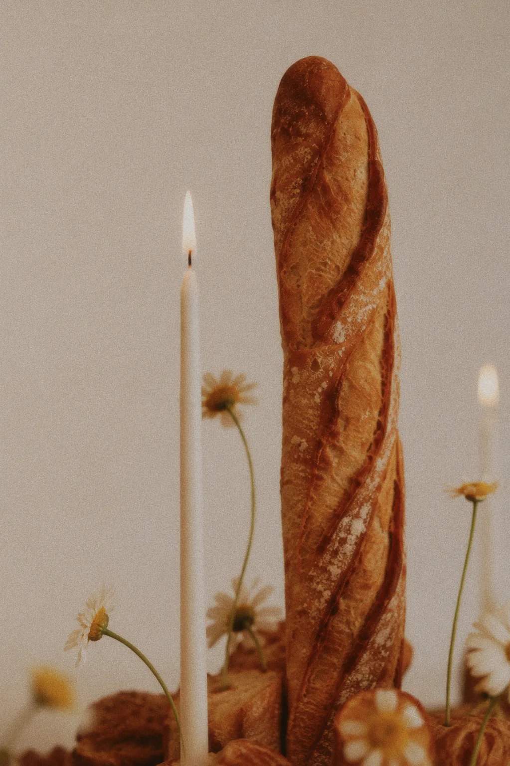 Tall scored baguette framed by lit white taper candles and delicate yellow flowers