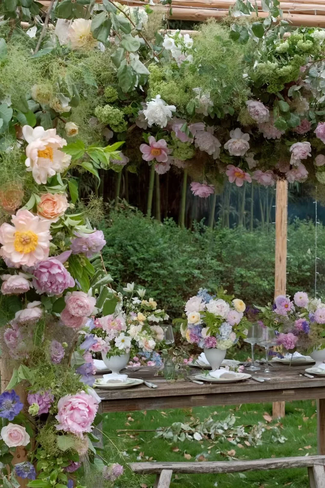 Garden reception table beneath a peony-laden arbor with pastel centerpieces
