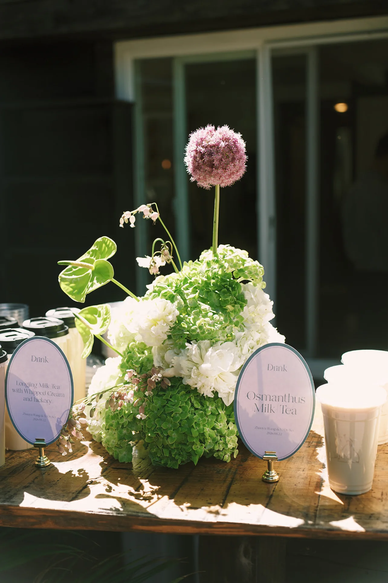 Sculptural green and white floral arrangement with a tall purple allium on an outdoor drinks table