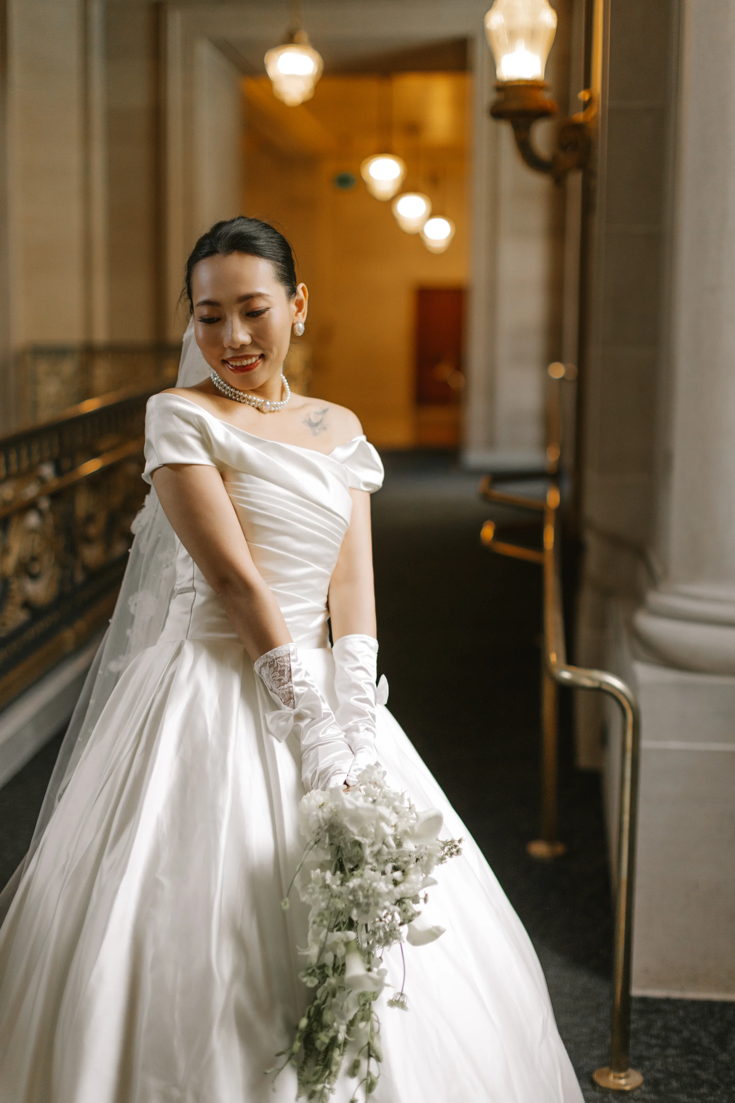 Bride on the grand staircase in a satin gown holding a cascading white bouquet