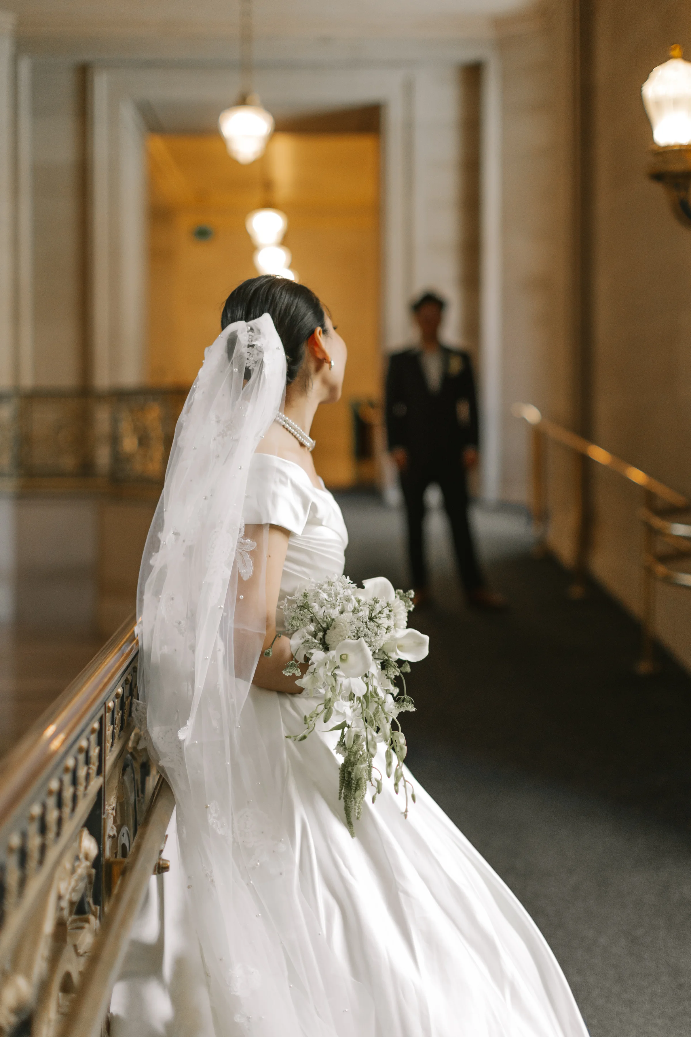 Bride on the staircase with the groom standing below in the background