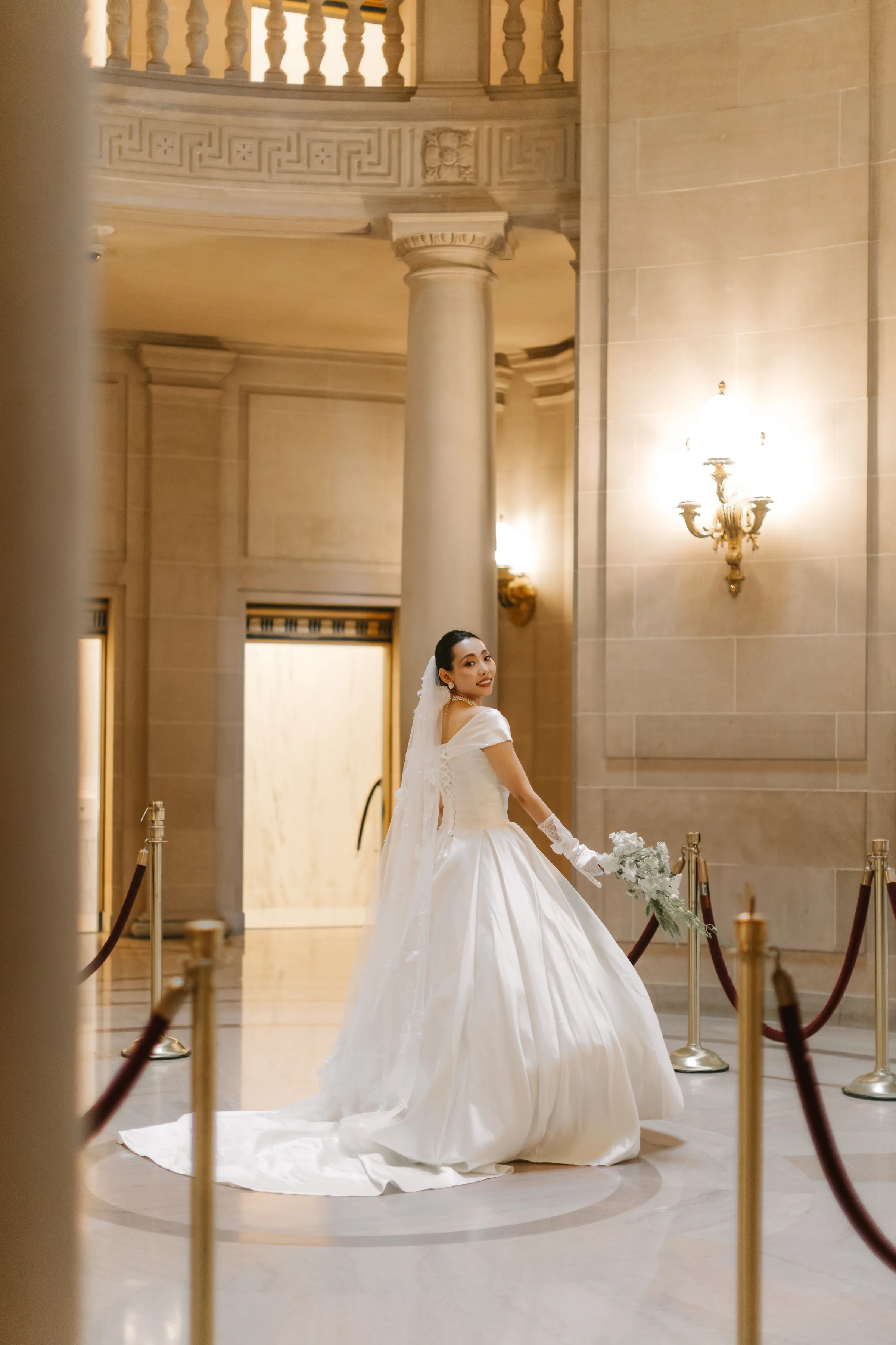 Bride descending a carpeted stair between stanchions in her satin gown