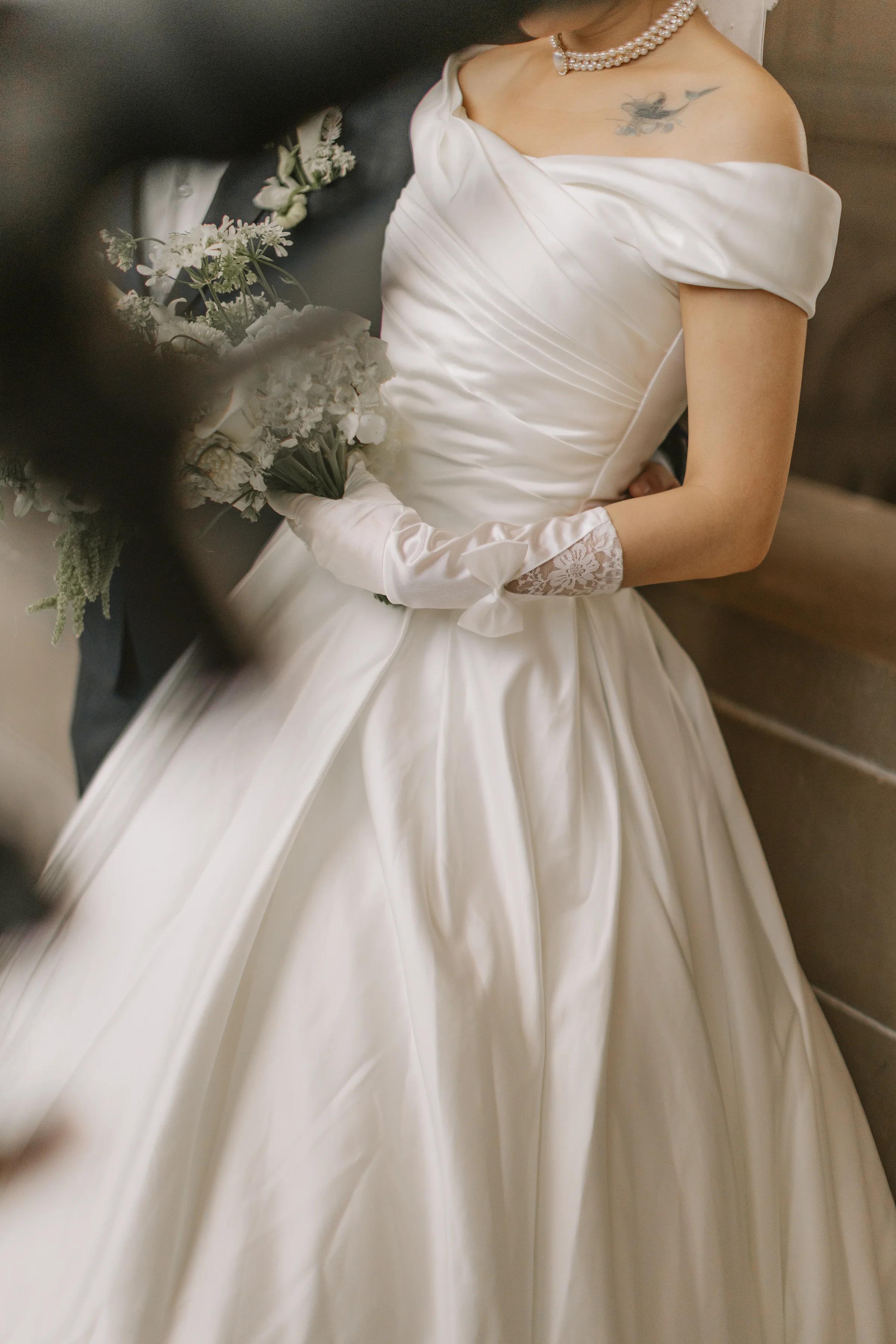 Bride in her satin off-shoulder gown holding a white bouquet in soft light
