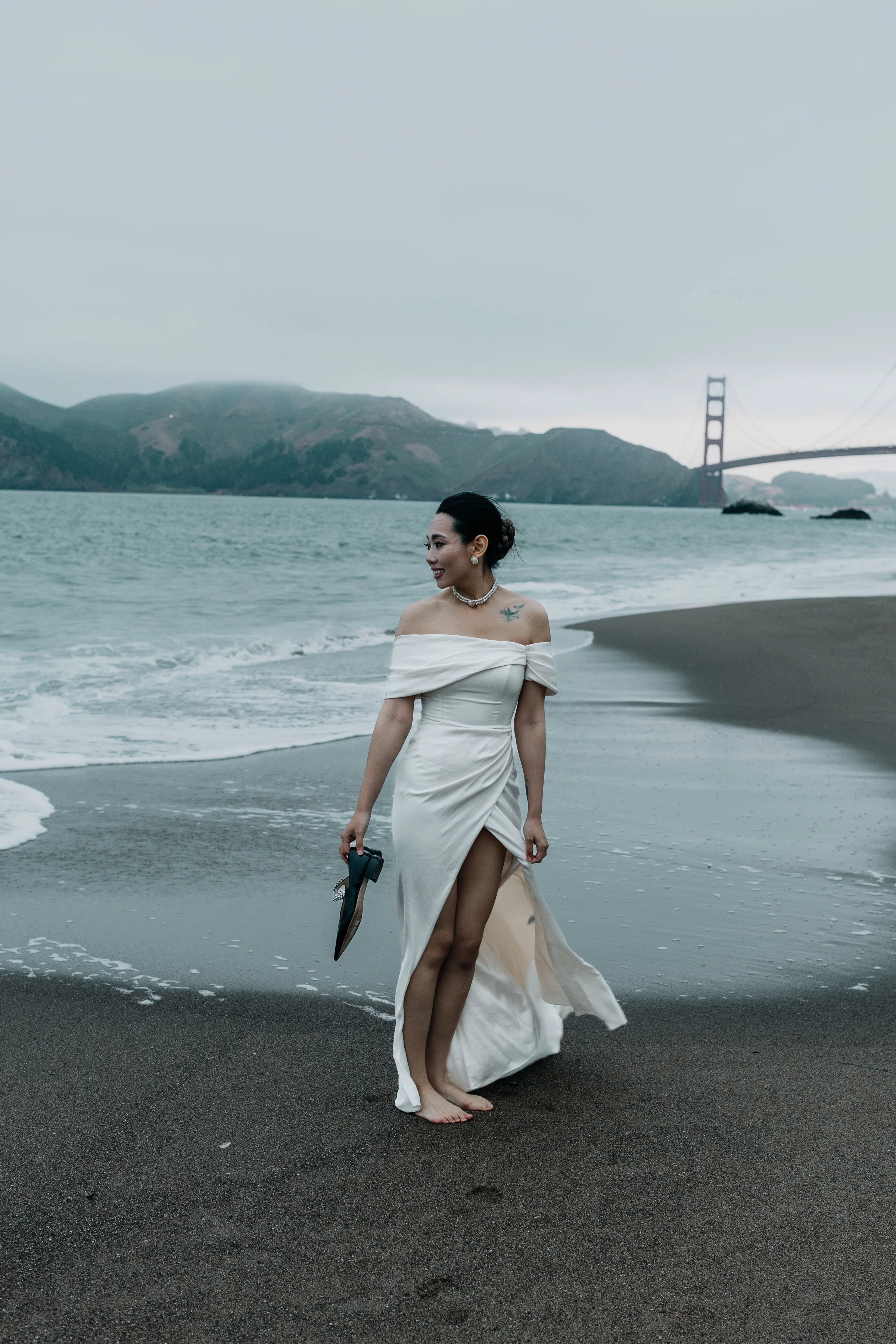 Bride in her gown walking the shoreline with the Golden Gate Bridge behind