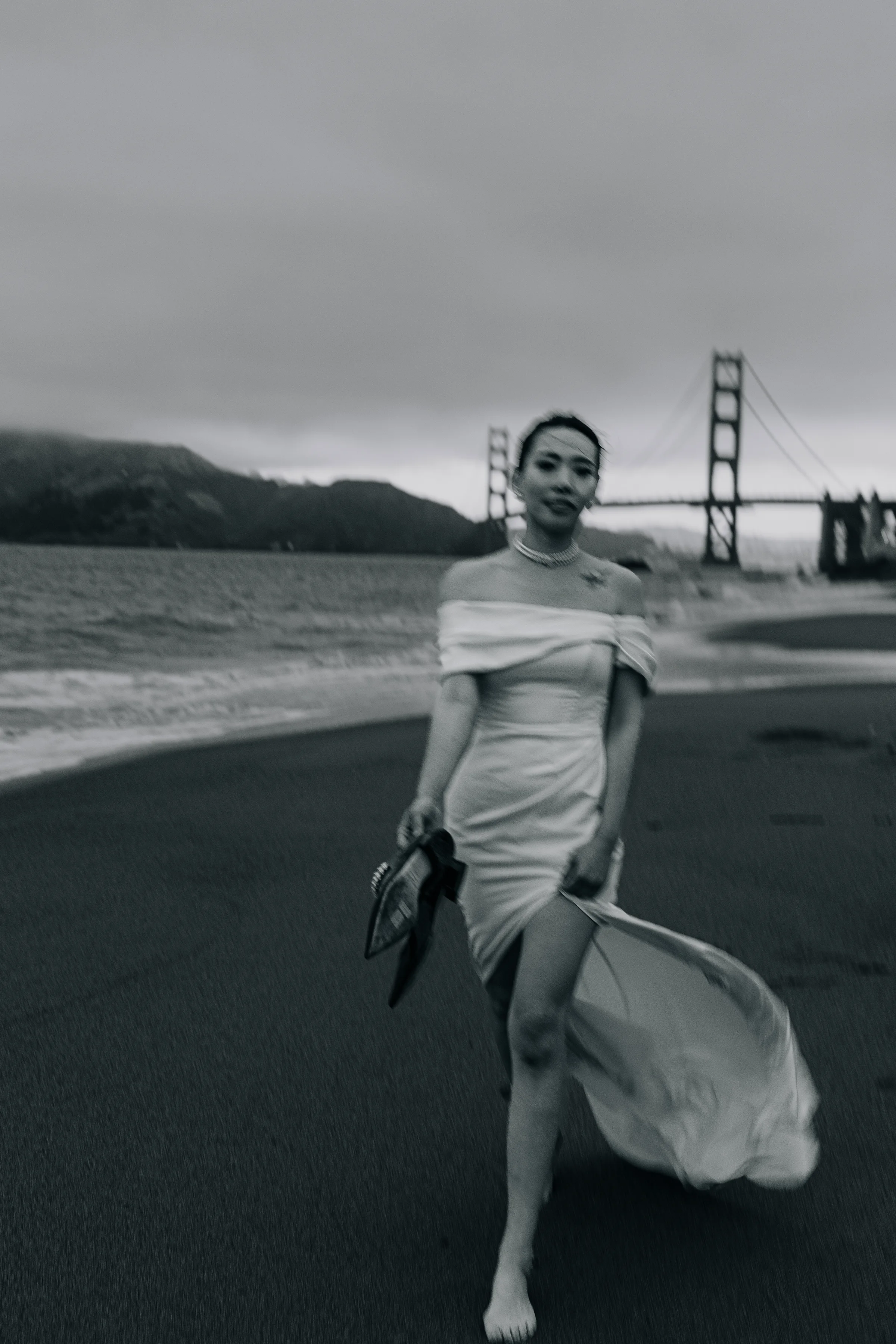 Black-and-white photo of the bride walking the beach, the Golden Gate Bridge behind