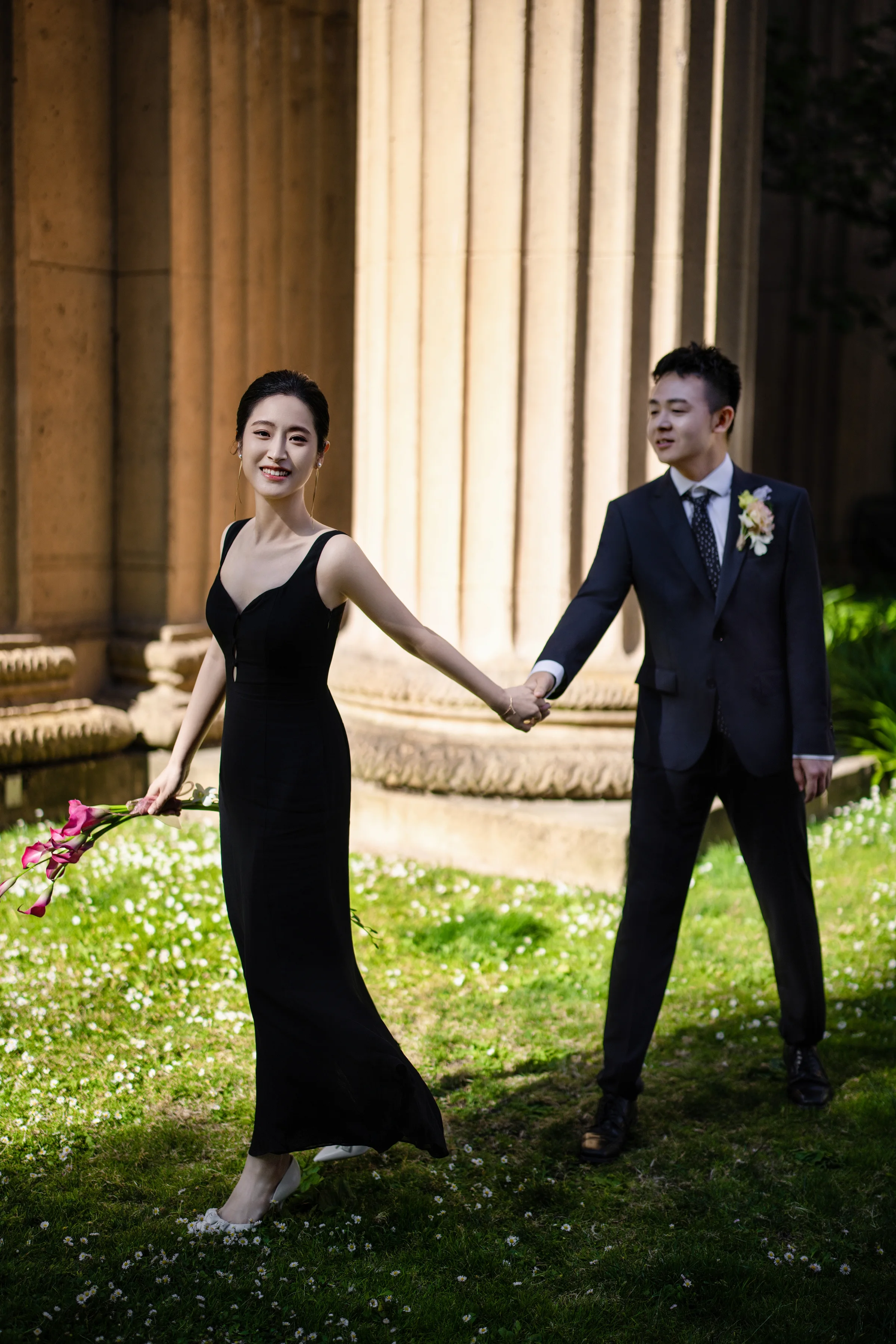 Couple holding hands on a lawn beside the Palace of Fine Arts columns