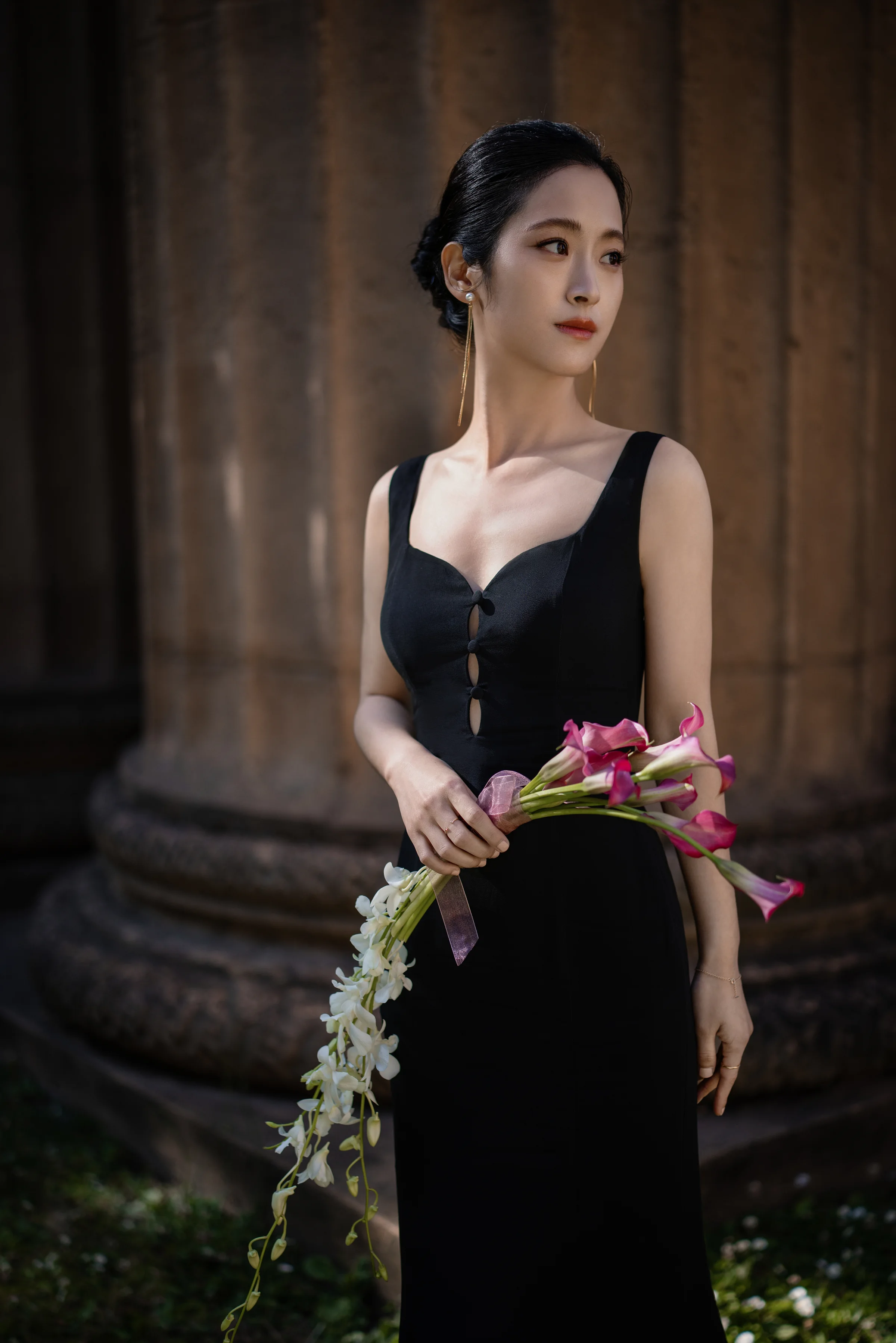 Bride standing by a fluted column holding a pink orchid stem