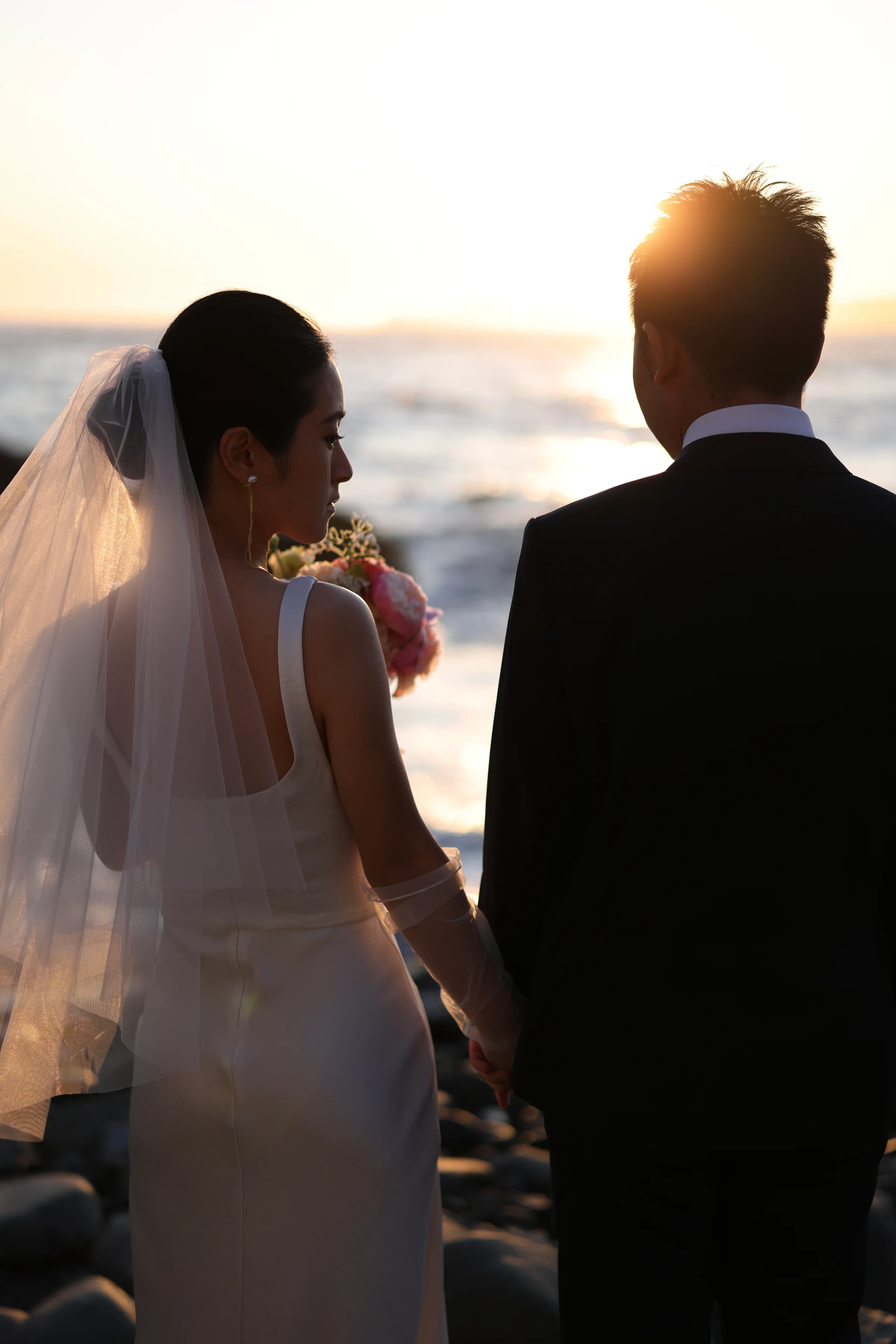 Couple backlit by sunset on the beach, the bride holding a colorful bouquet