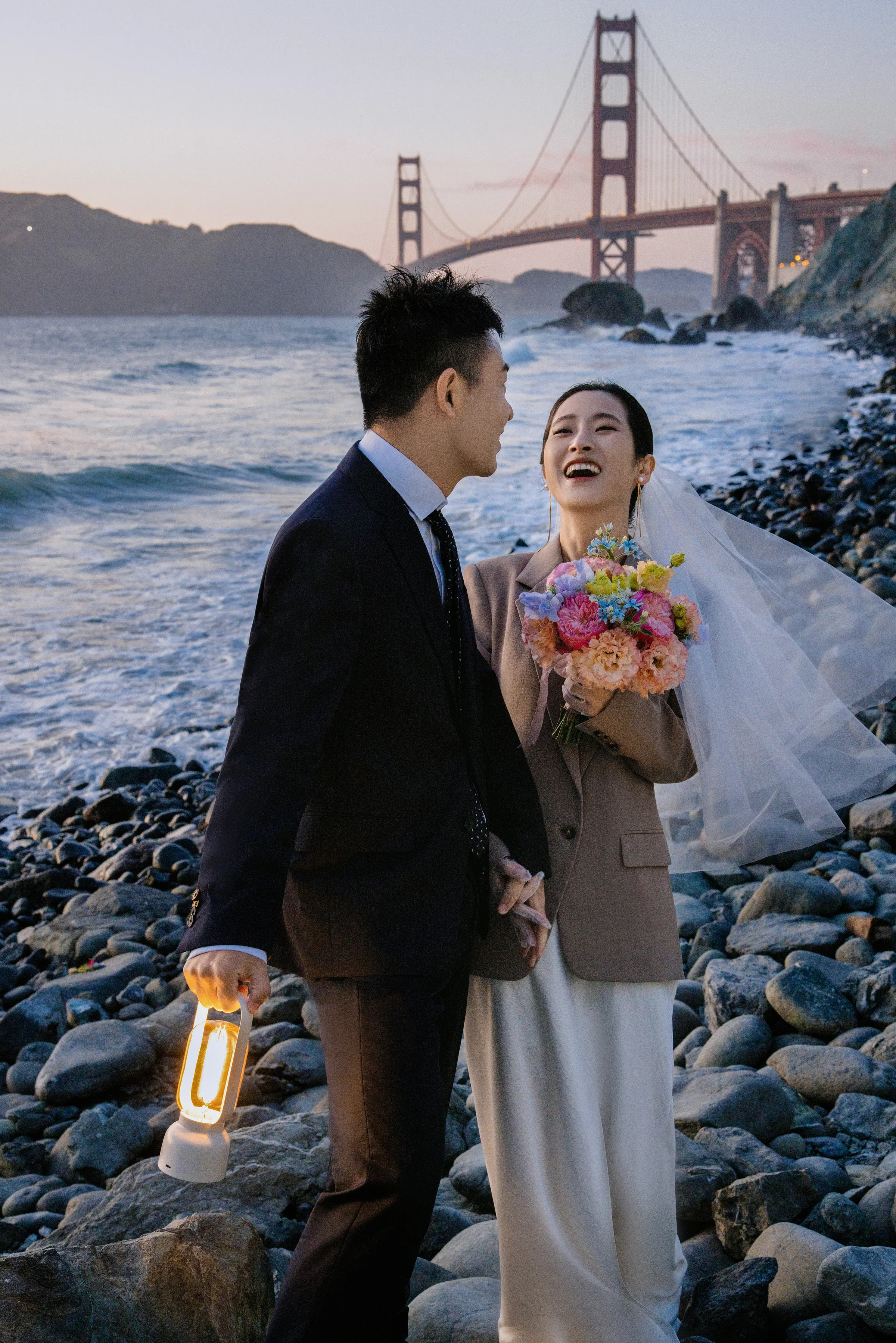 Couple standing on the rocks with the Golden Gate Bridge behind at dusk