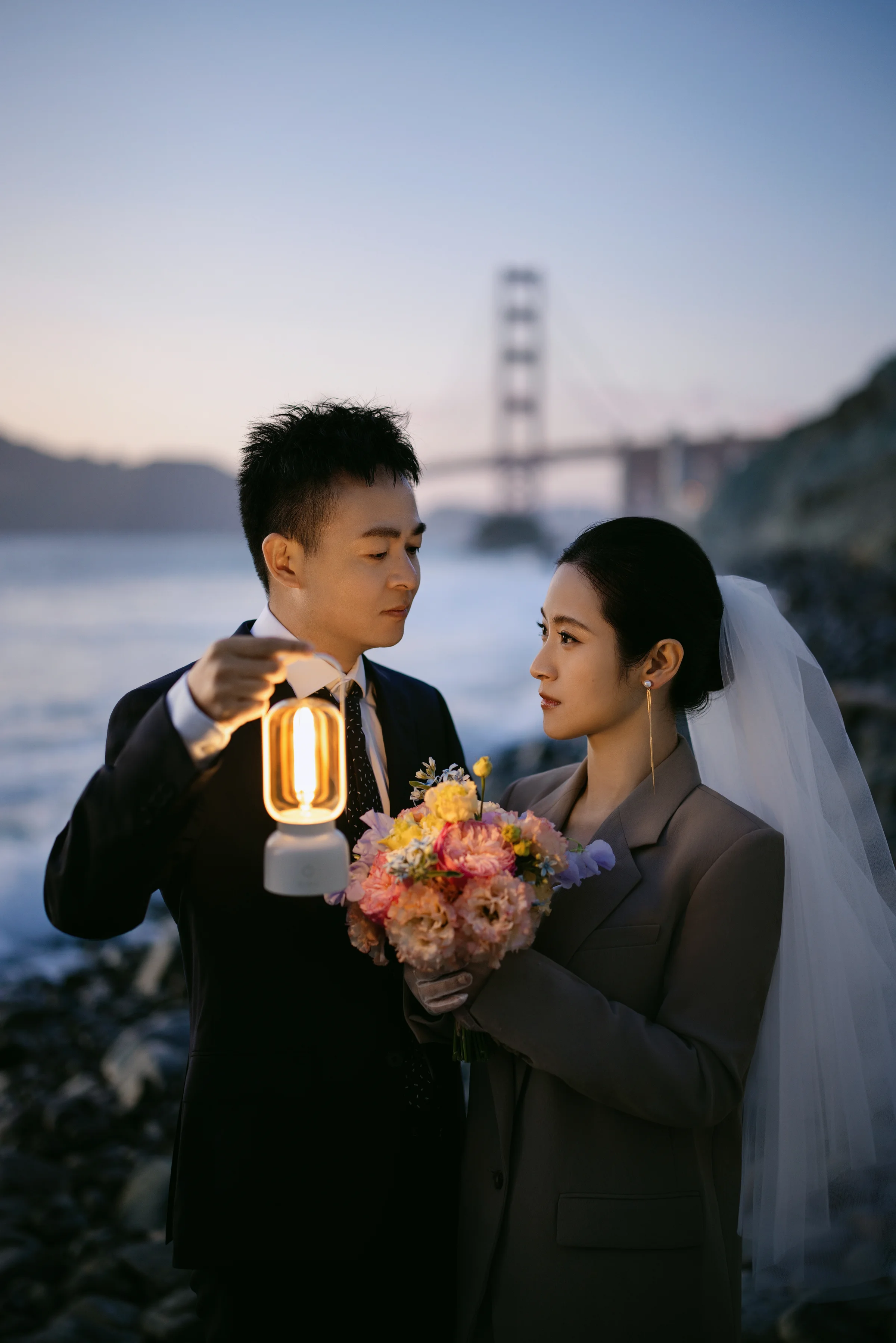 Groom holding a glowing lantern beside the bride, the Golden Gate Bridge behind