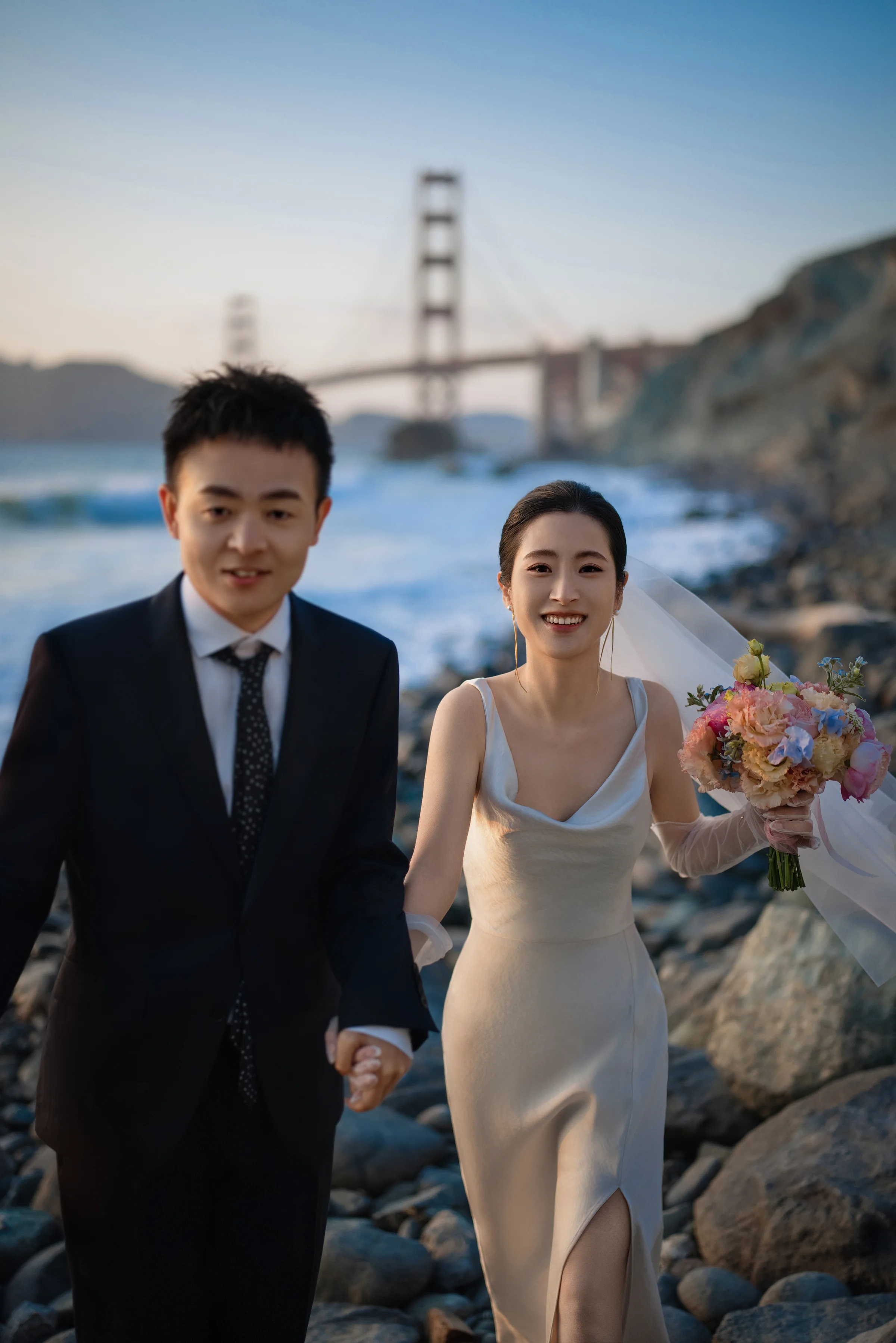 Couple holding hands on the beach with the Golden Gate Bridge behind