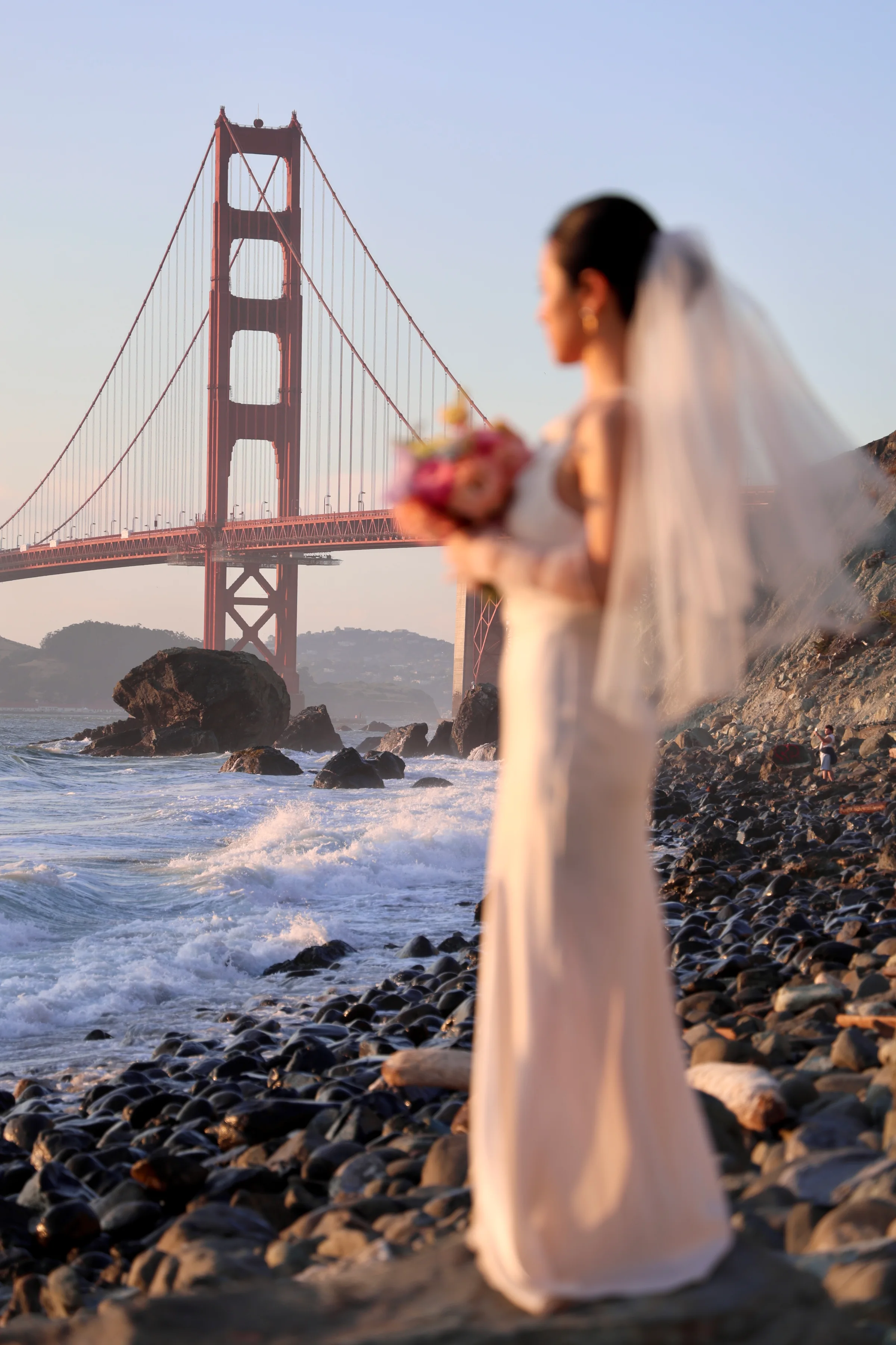 Bride with veil and bouquet gazing toward the Golden Gate Bridge