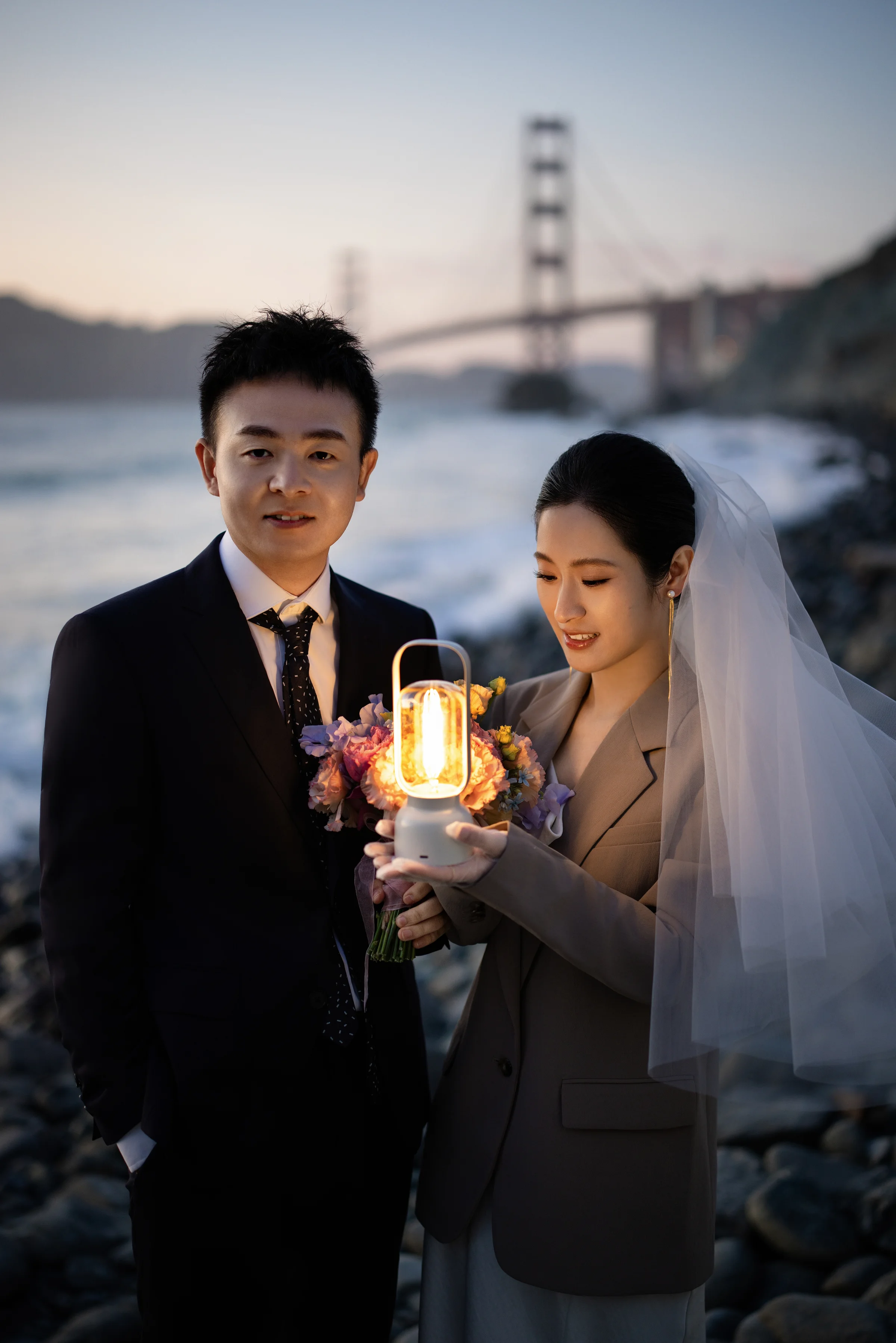 Couple close together at sunset, the bride holding a pastel bouquet with the Golden Gate Bridge behind