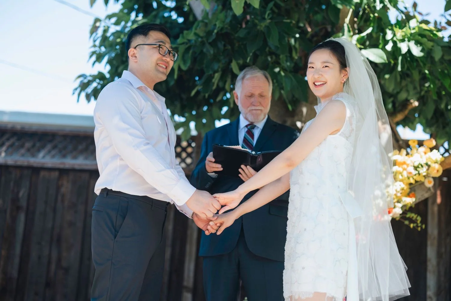Couple holding hands and laughing during their backyard ceremony as the officiant reads