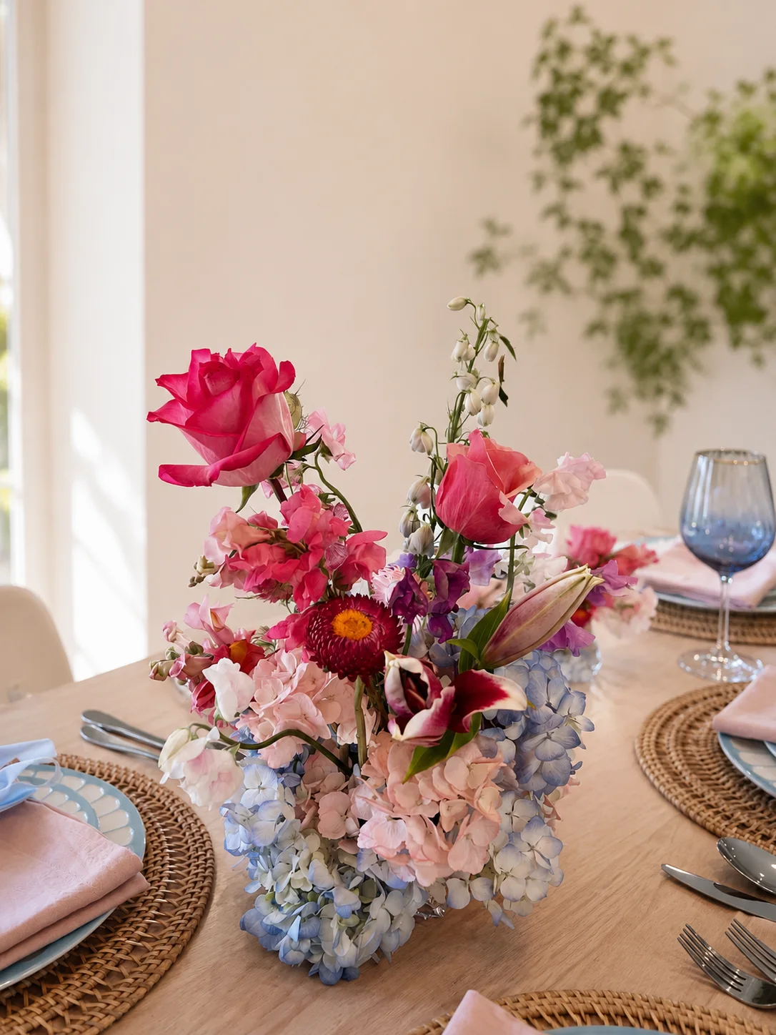 Pink rose, sweet pea, and blue hydrangea centerpiece on a sunlit styled table