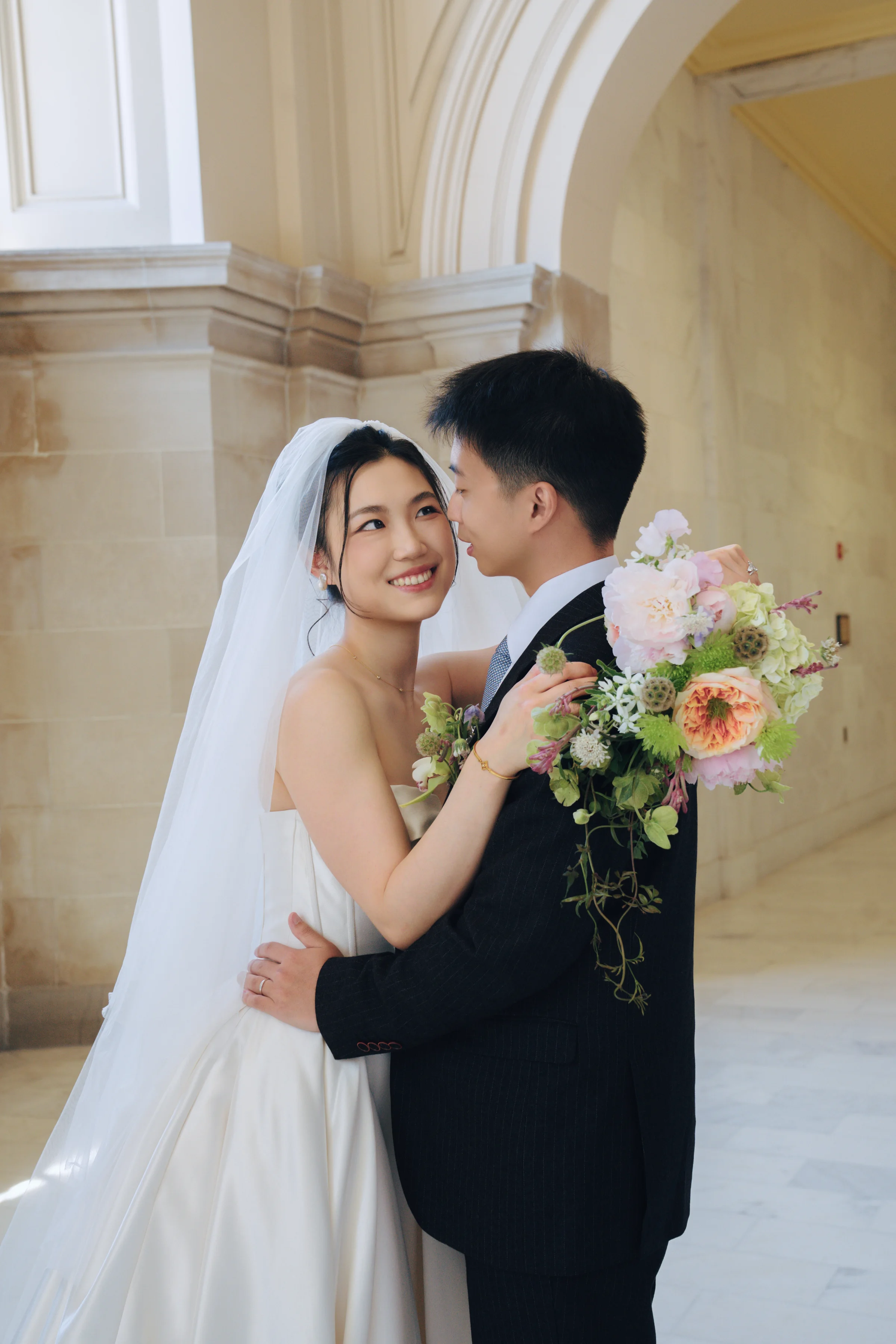 Couple embracing by an archway, the bride holding her bouquet