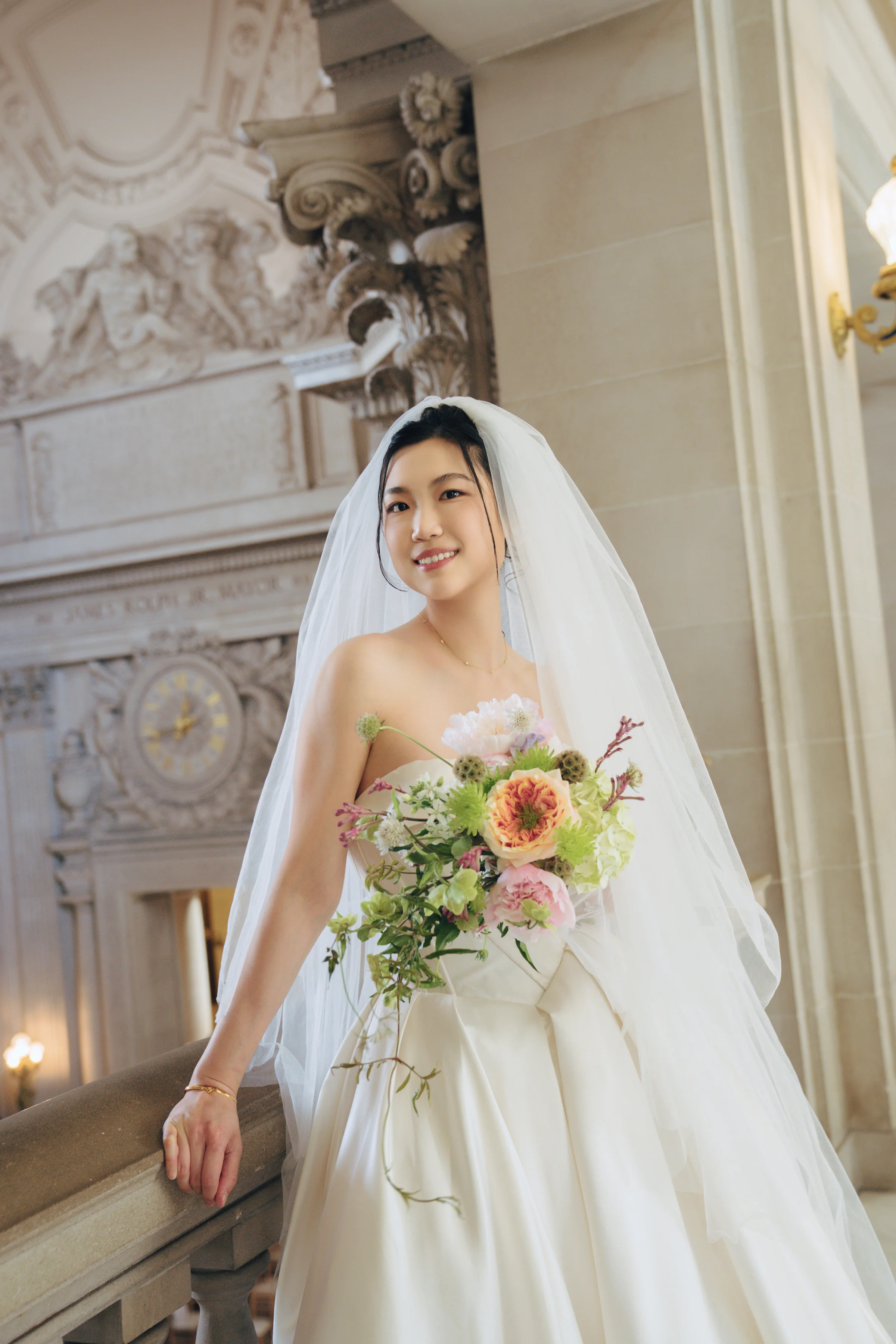 Bride leaning on a balustrade with her bouquet beneath ornate carving