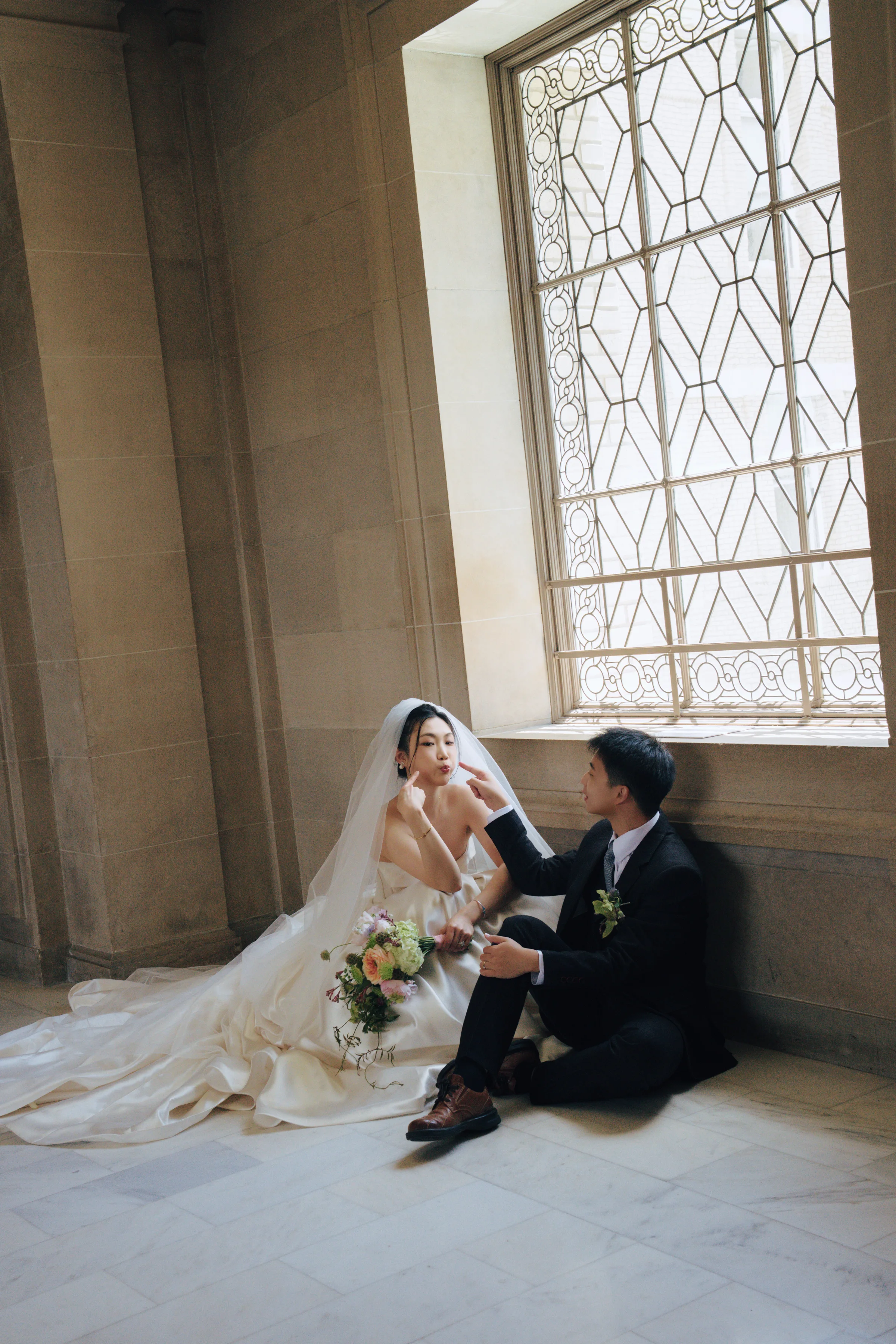 Couple seated on the floor by a tall lattice window, softly backlit