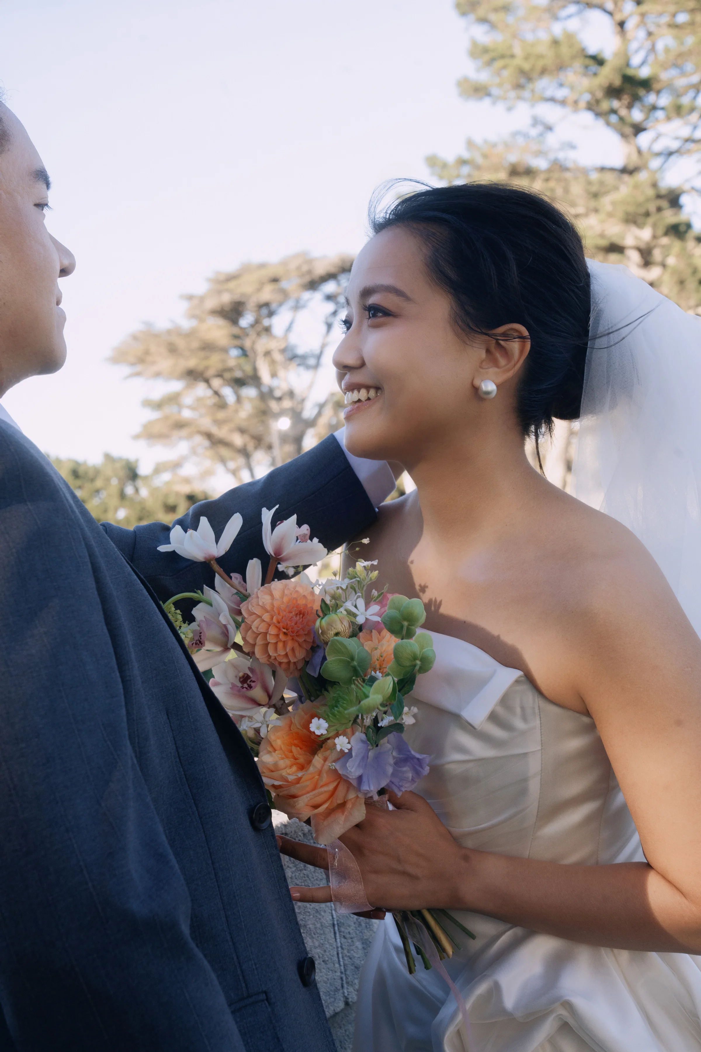 Bride smiling closely with the groom while holding a peach and orange bouquet