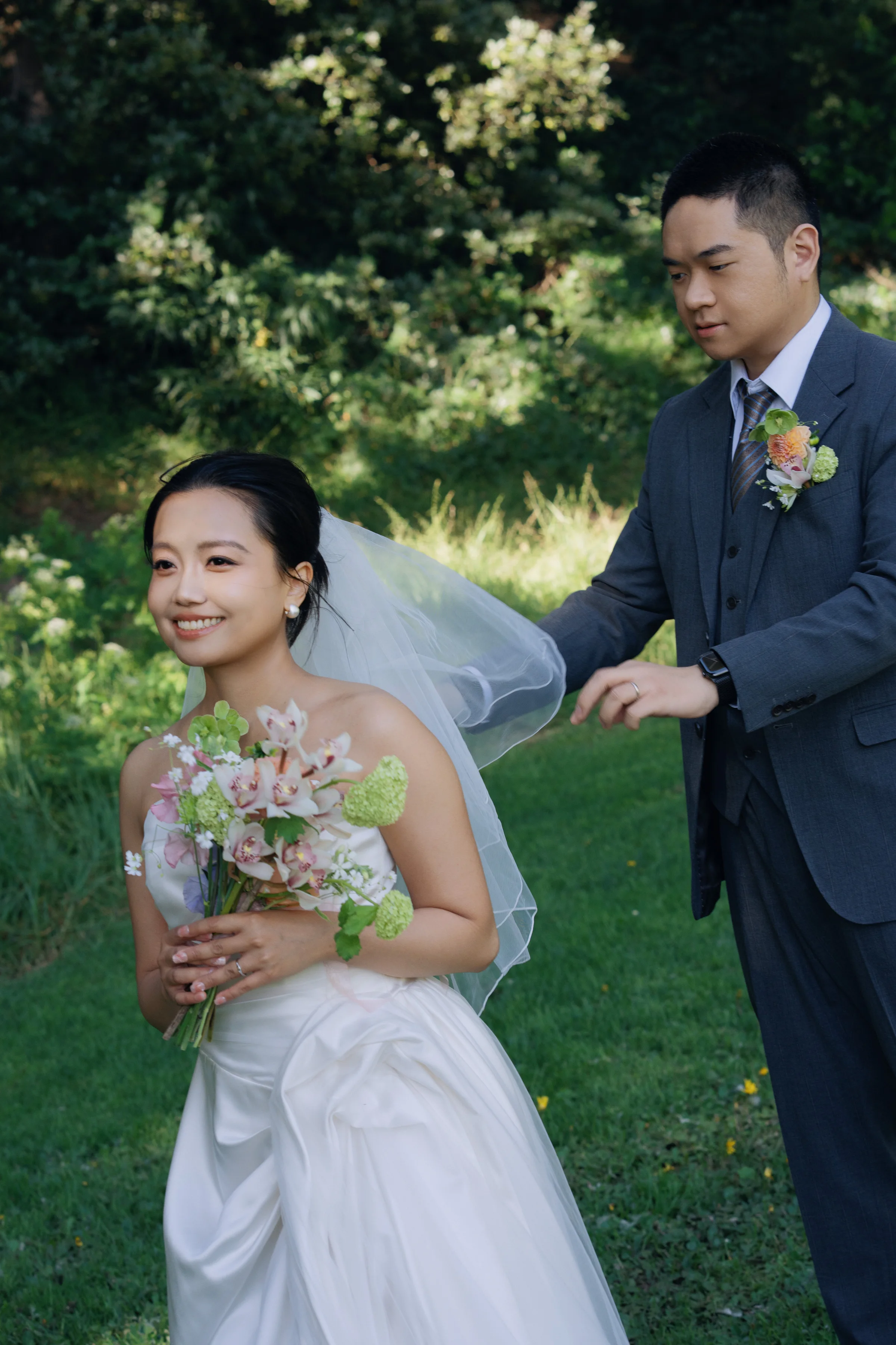 Groom taking the bride's hand as she holds a bouquet on a garden lawn