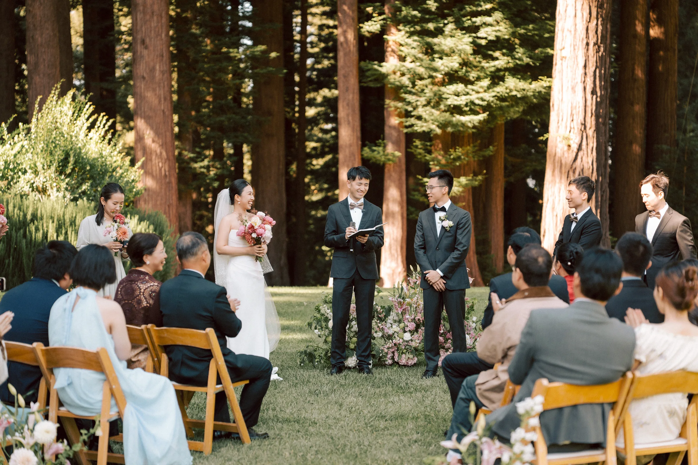 Outdoor ceremony in progress among the redwoods with seated guests