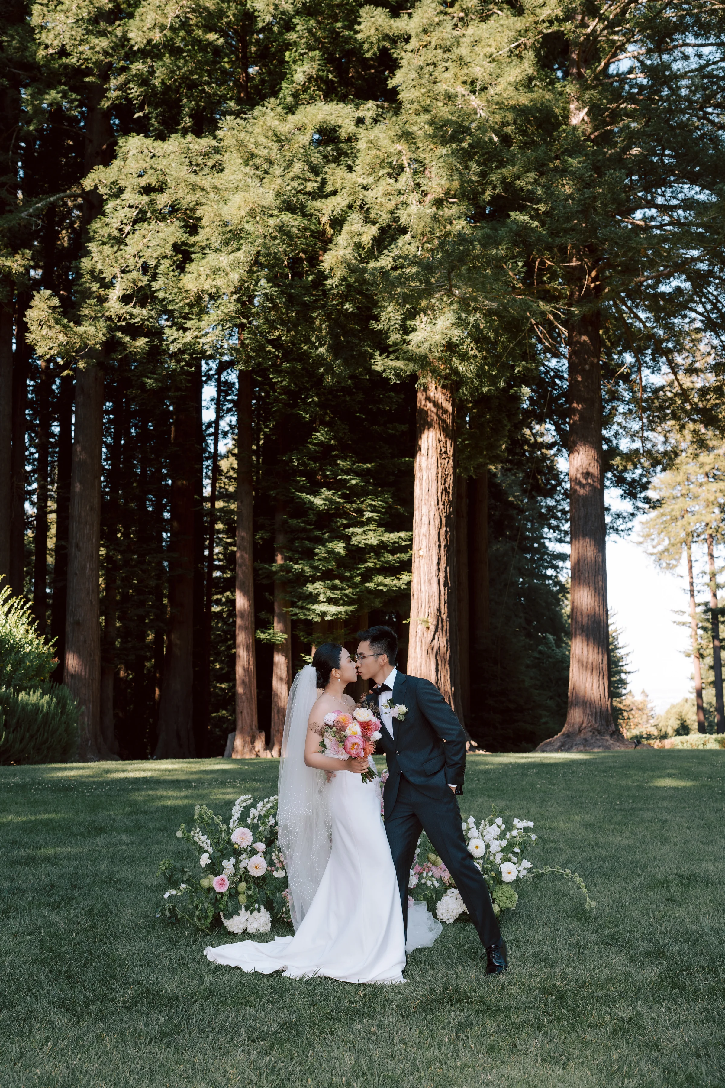 Couple celebrating in a sunlit clearing, the groom raising his arm near a floral installation
