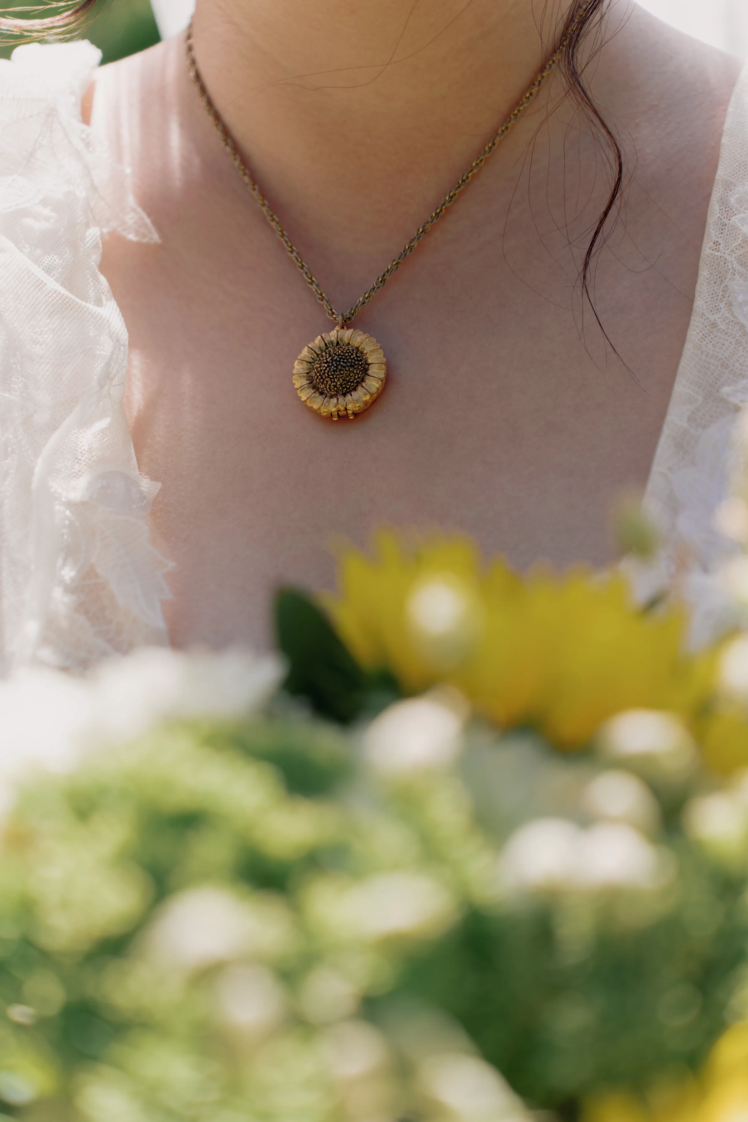 Close-up of the bride's sunflower pendant above her softly blurred yellow and green bouquet.