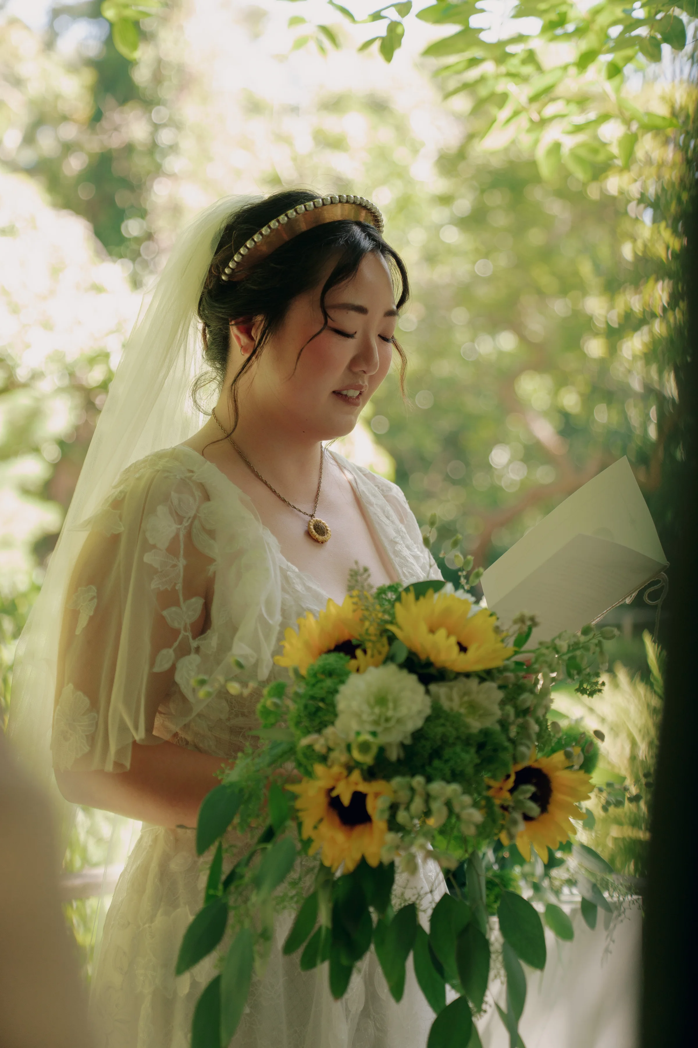 Bride reads a letter while holding a lush bouquet of sunflowers, white flowers, and greenery.