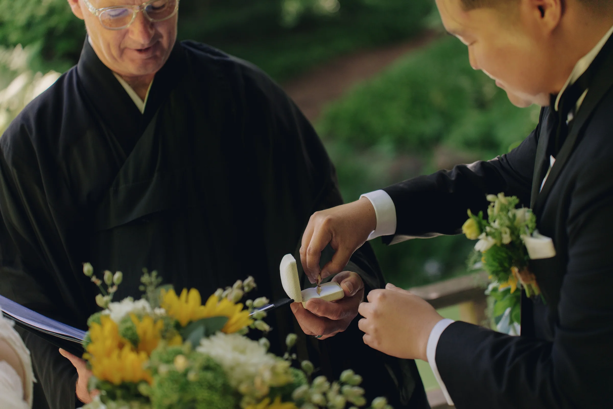 Groom places a wedding ring into an open ring box during the garden ceremony.