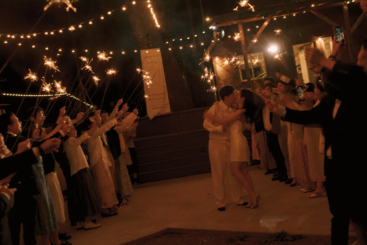 Newlyweds kissing as guests hold sparklers along both sides of the nighttime reception.