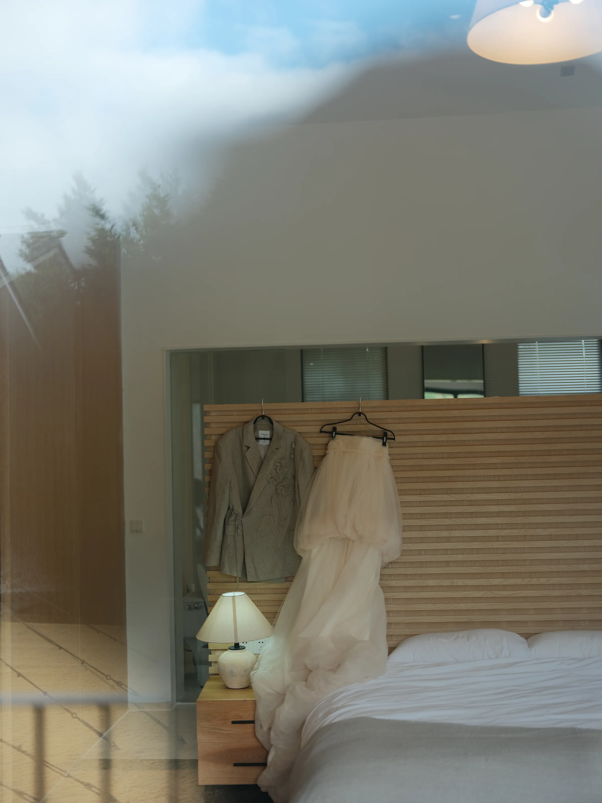 Getting-ready suite with the wedding dress hanging by a window above a made bed