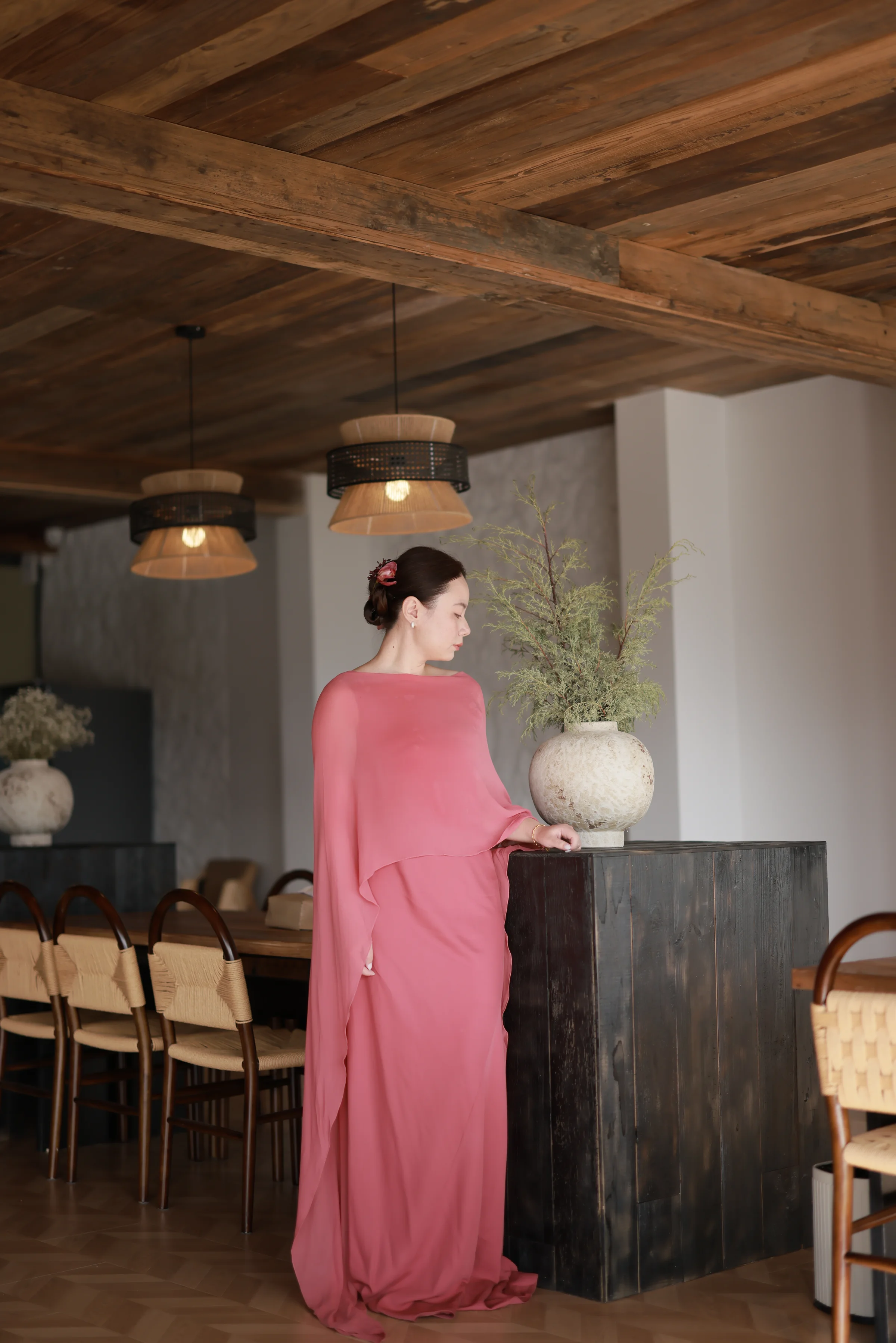 Bride in a long coral dress standing in a warm wood-paneled dining room