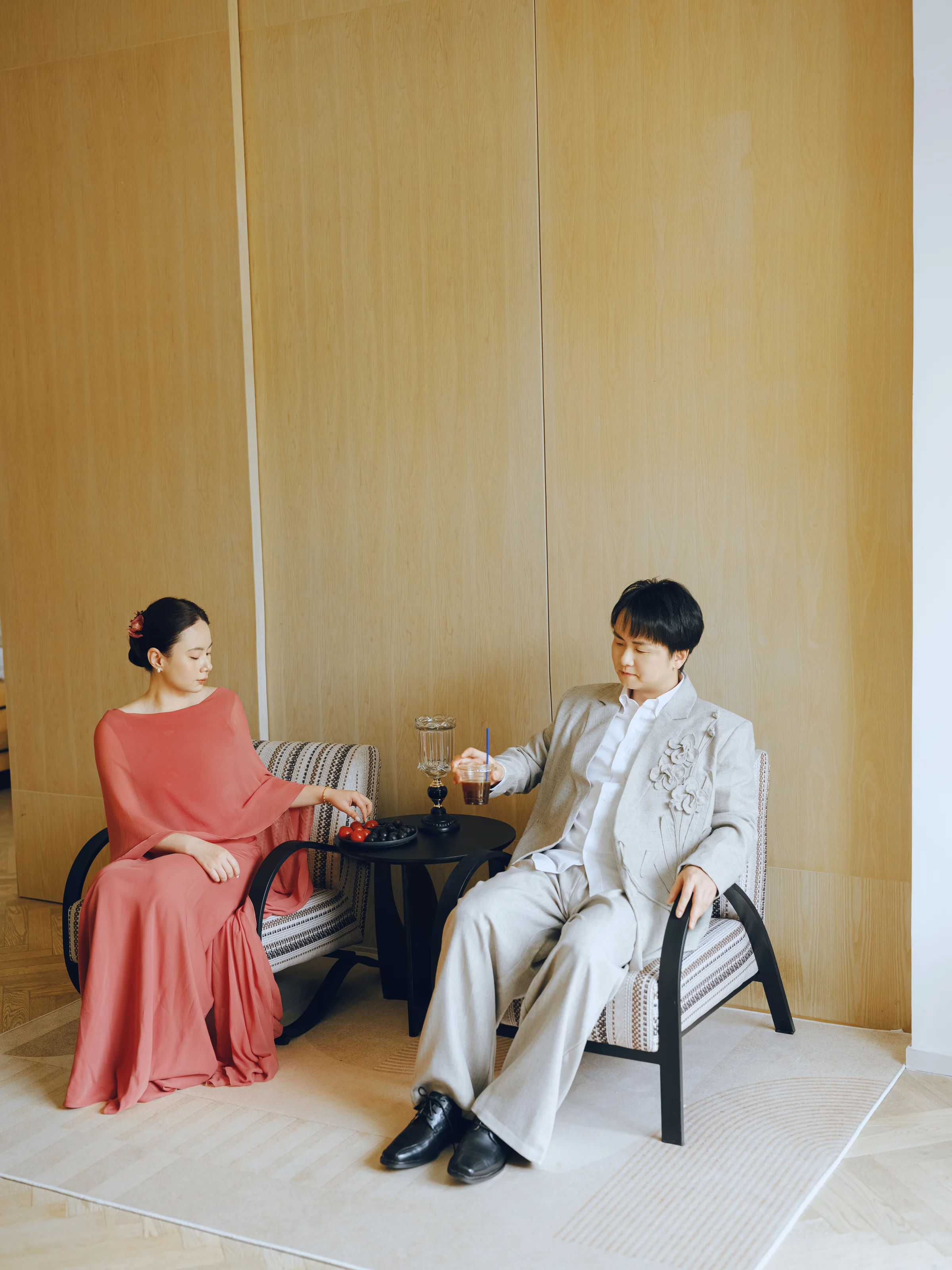 Bride in coral and groom in cream seated together in a softly lit interior