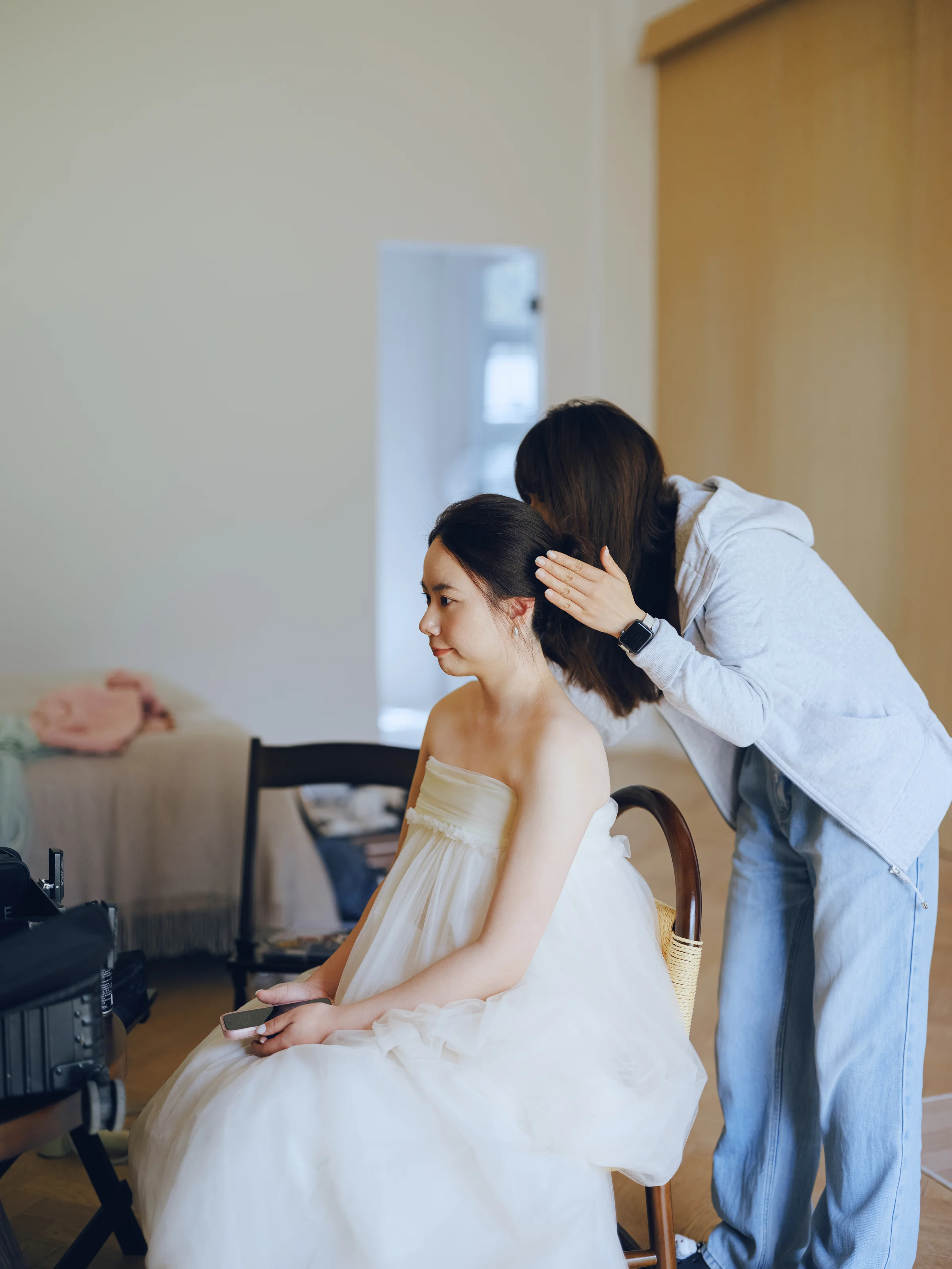Groom adjusting the seated bride's hair as she wears her white gown