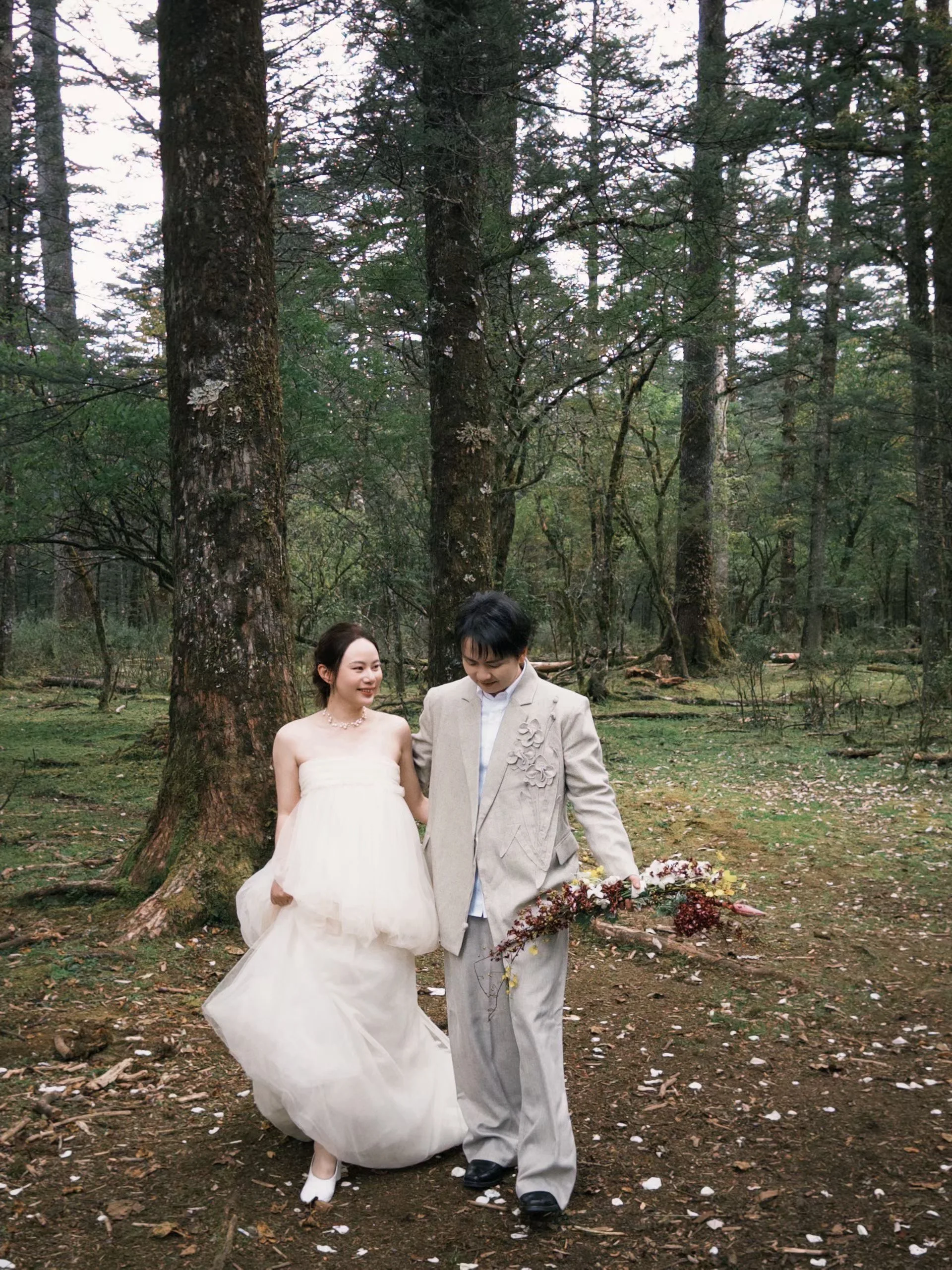 Couple walking a wooded path, the bride holding an autumnal bouquet