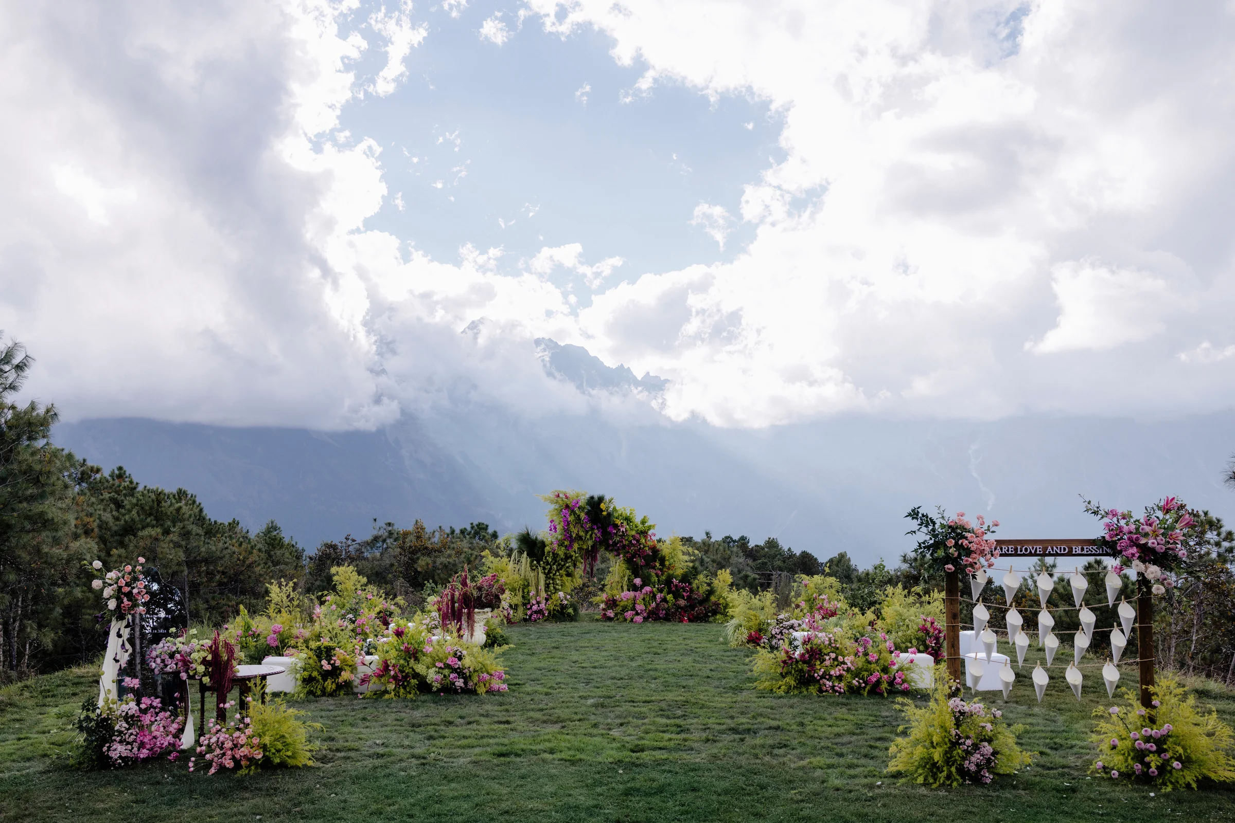 Ceremony set on a lawn with a floral arch and seating beneath a dramatic mountain sky