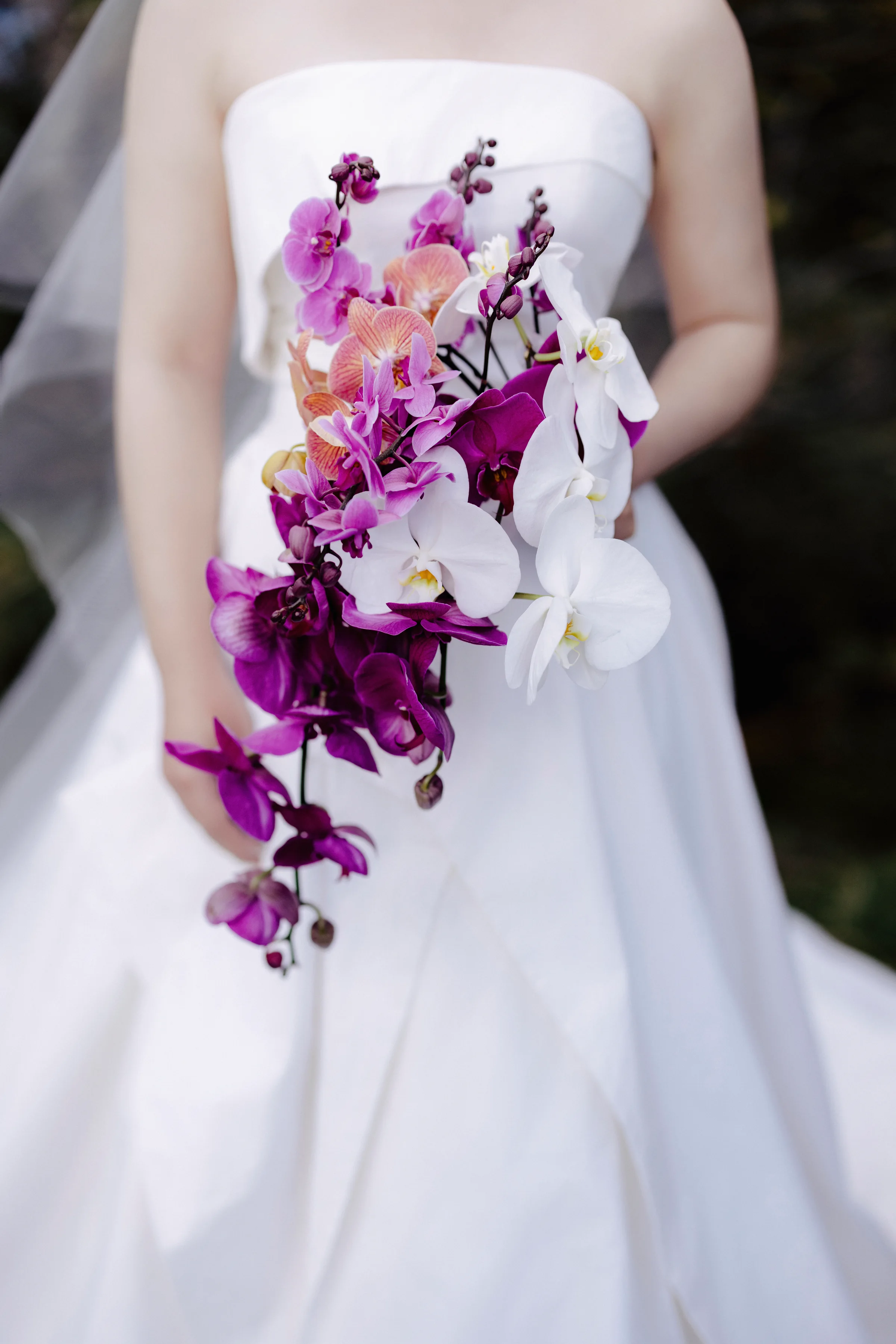 Bride holding a bouquet of purple and white orchids against her white gown
