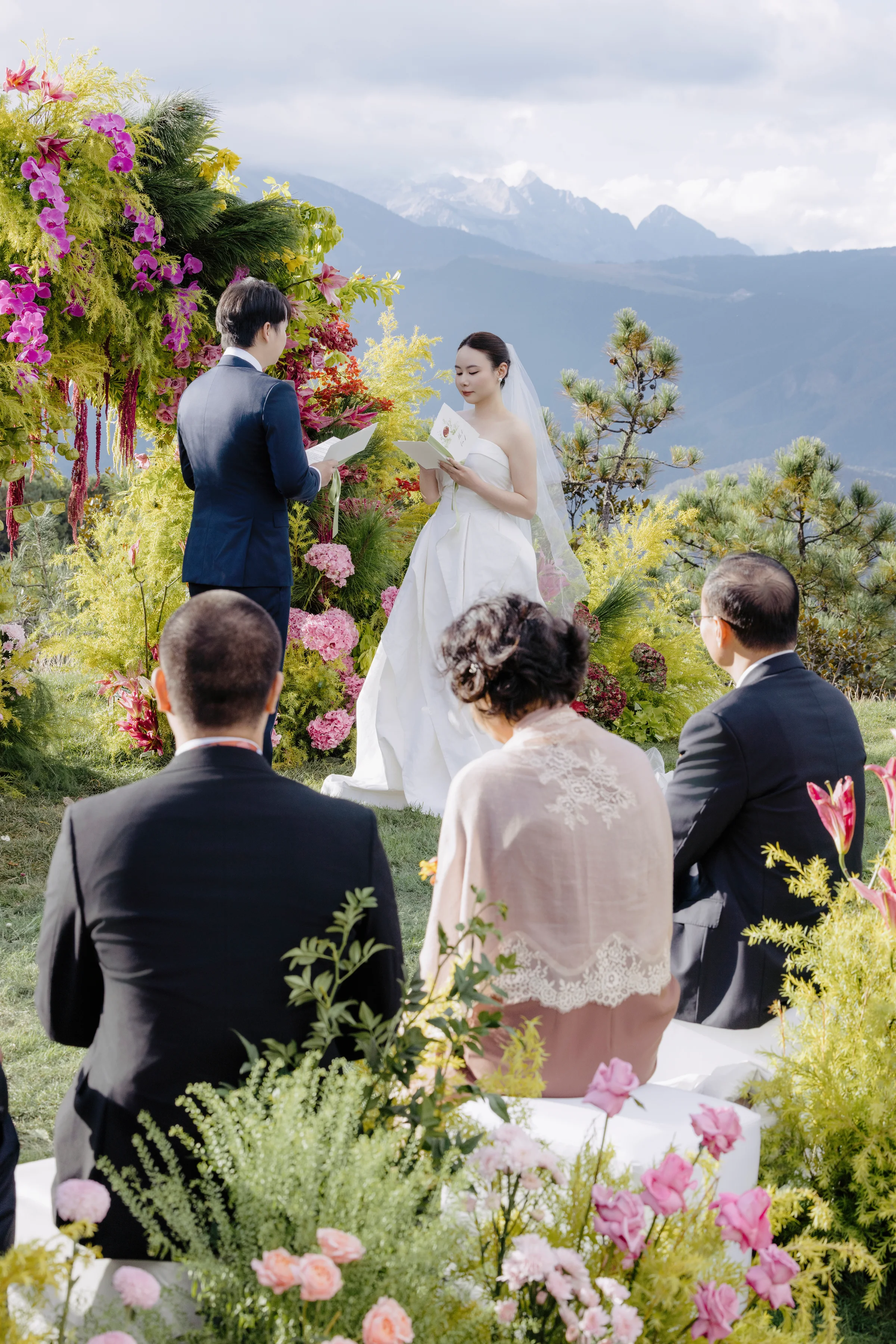 Outdoor ceremony in progress with floral arches, guests, and a mountain backdrop