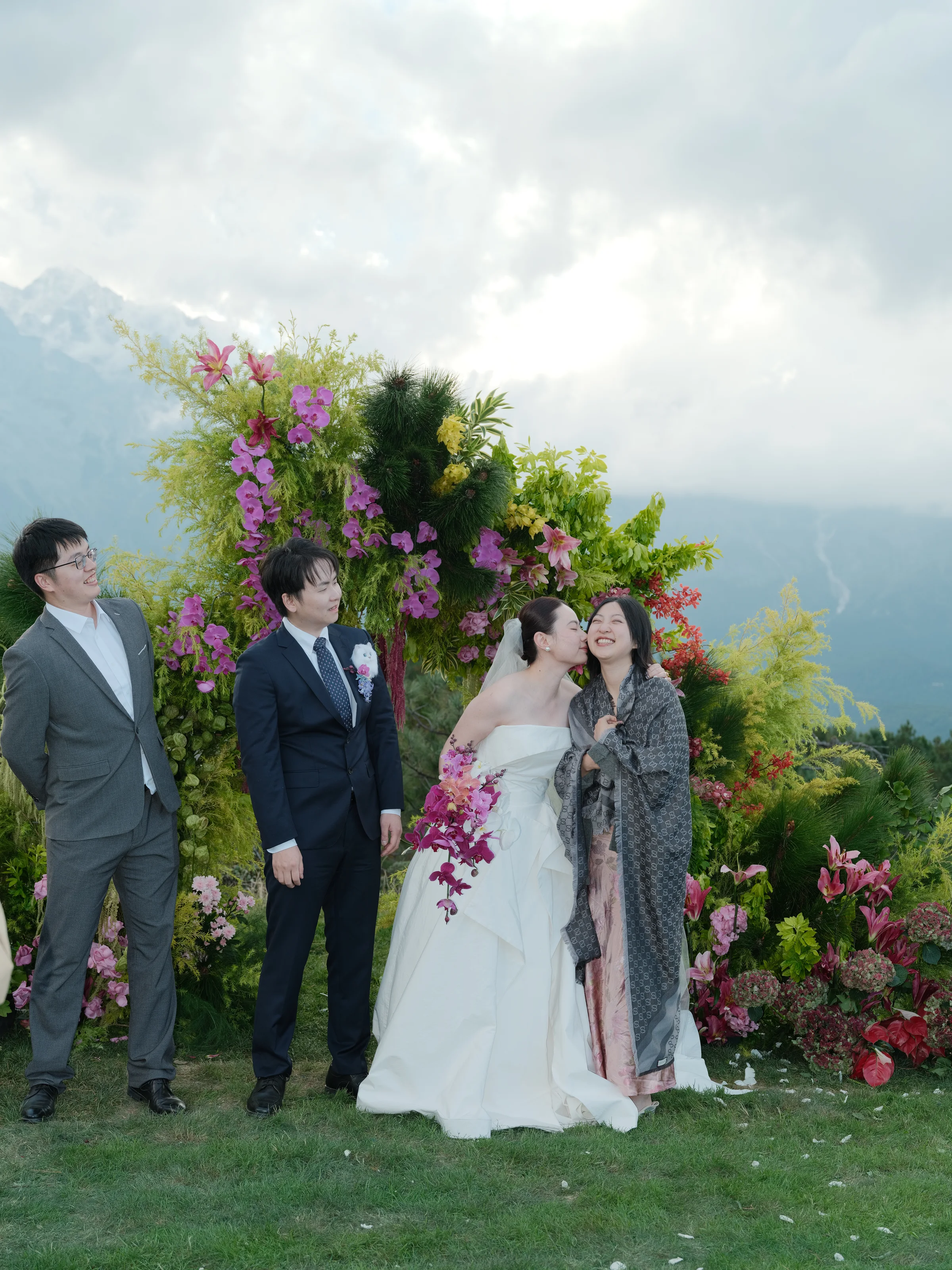 Couple with two guests beside a floral arch and mountain view