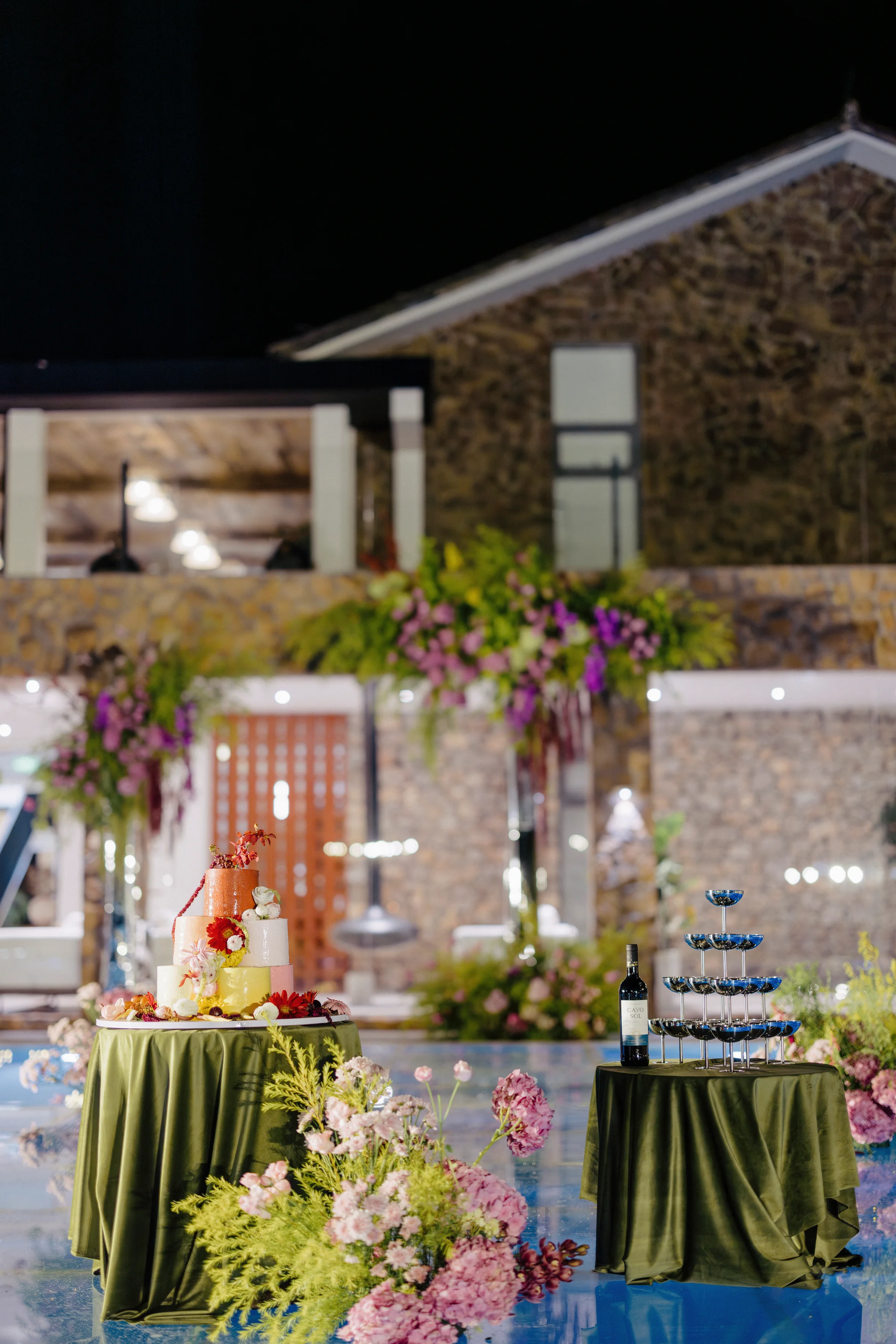 Evening reception courtyard with a cake, florals, and a stone building