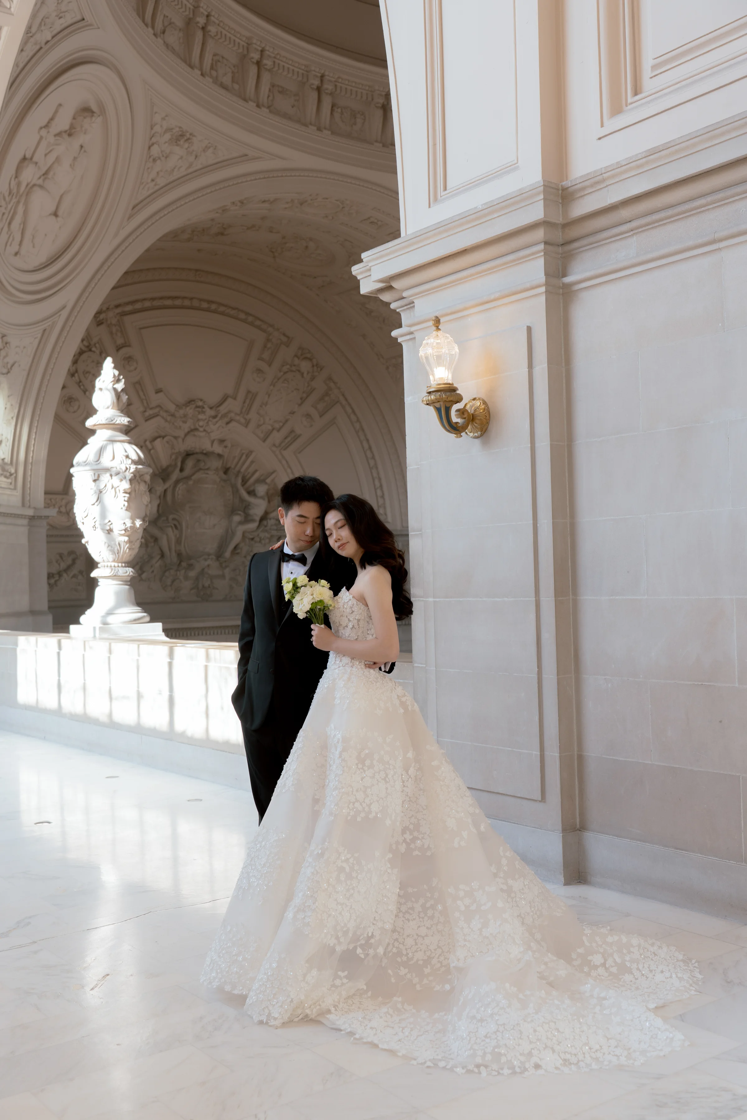 Couple embracing beside a tall marble urn by an arched window