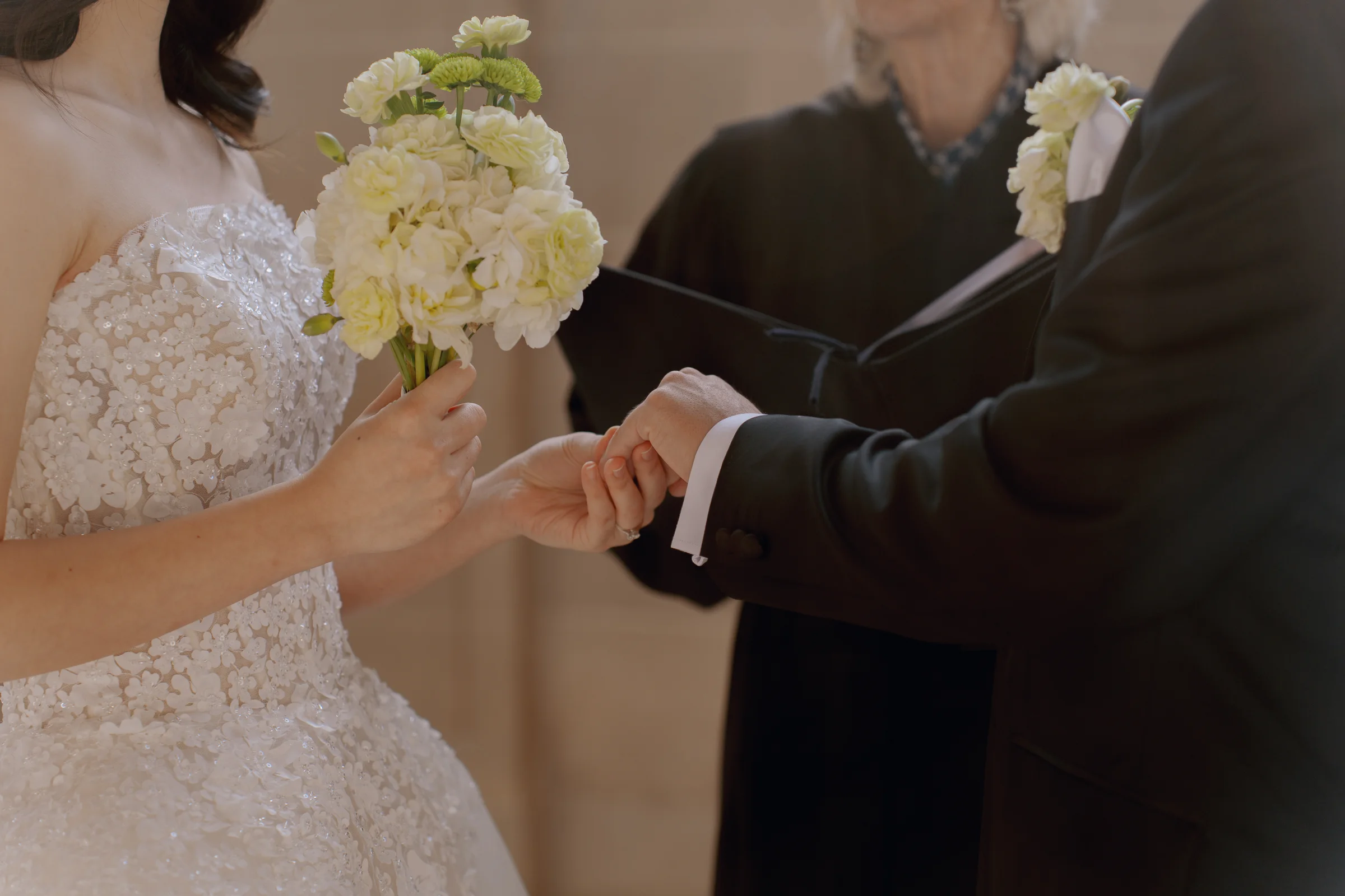 Close-up of the ring exchange as the bride holds a pale bouquet